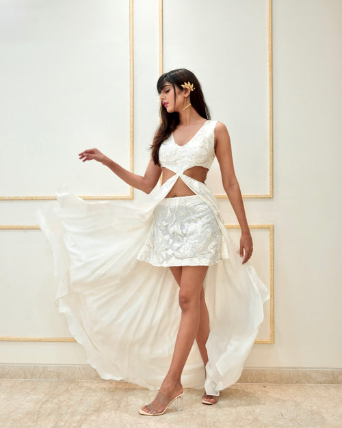 Woman in a white dress with cut-out design against a light-colored wall.