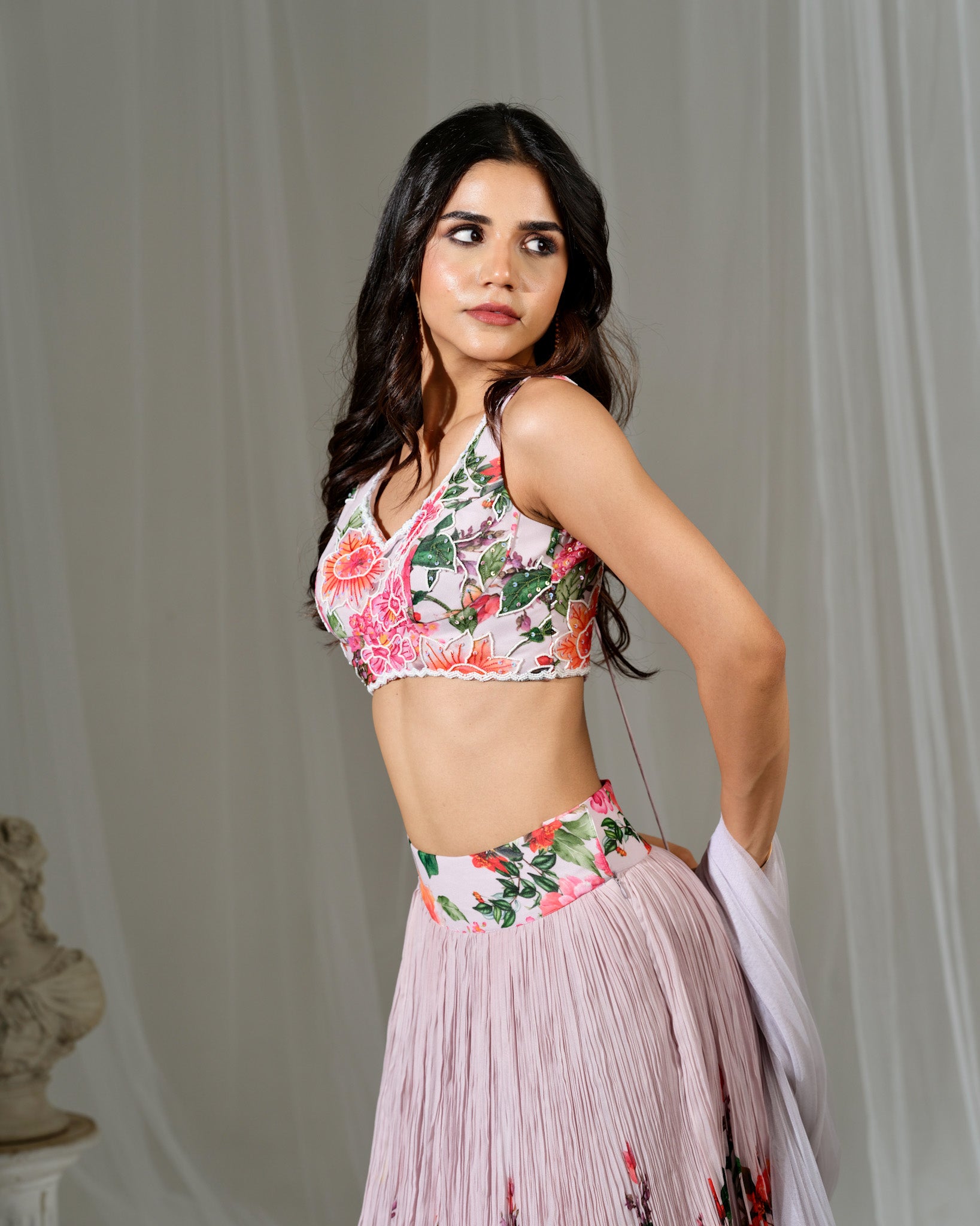 Woman wearing a floral top and pink skirt against a neutral background