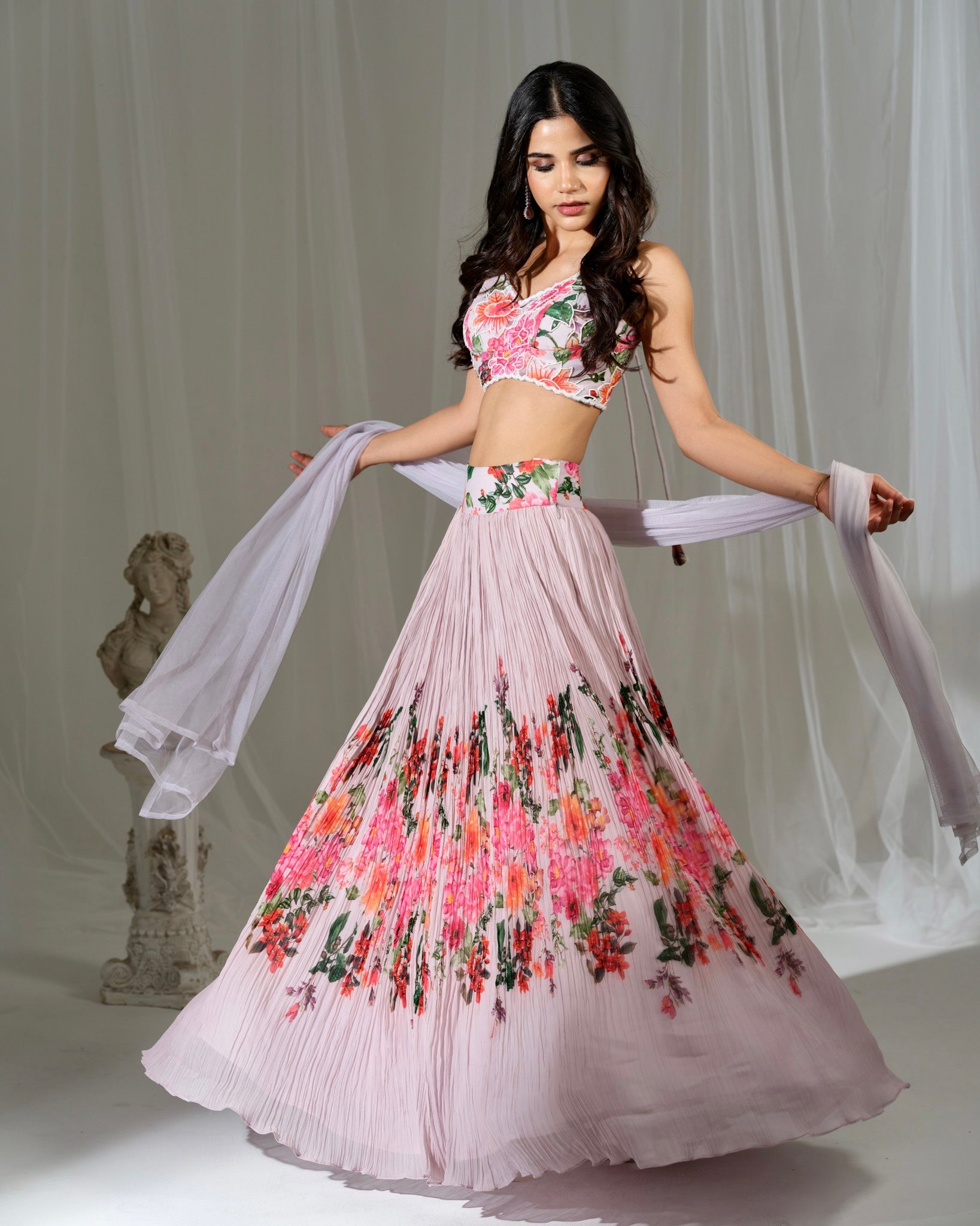Woman wearing a floral pink lehenga with a white blouse against a neutral background