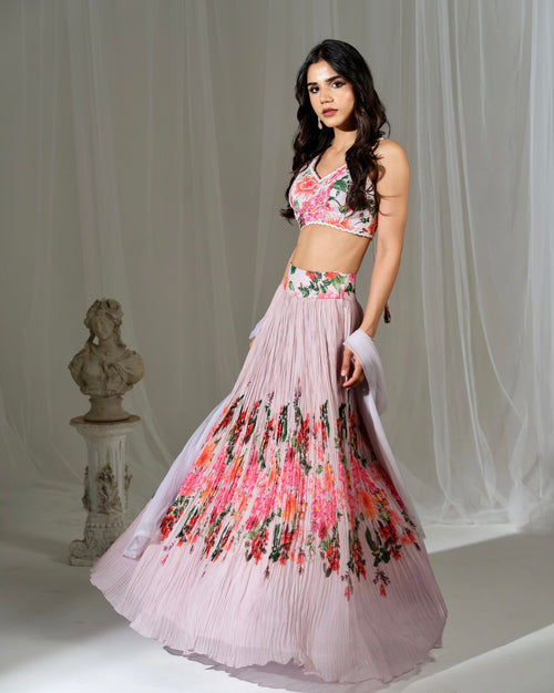 Woman wearing a floral dress with a bustier top and pleated skirt against a white curtain background.