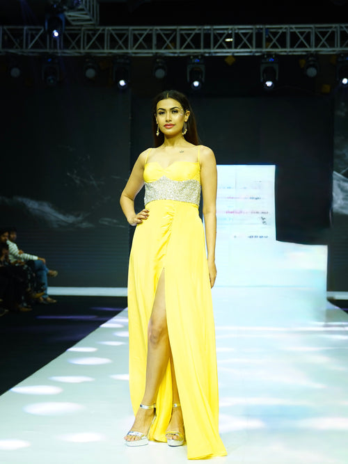 Model wearing a yellow evening gown with a silver belt on a runway.