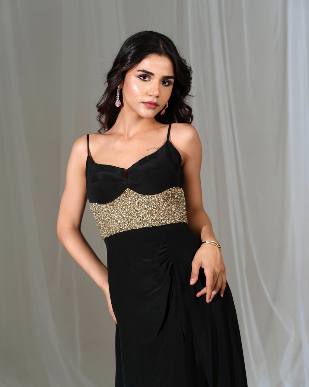 Woman wearing a black and gold evening gown against a gray background