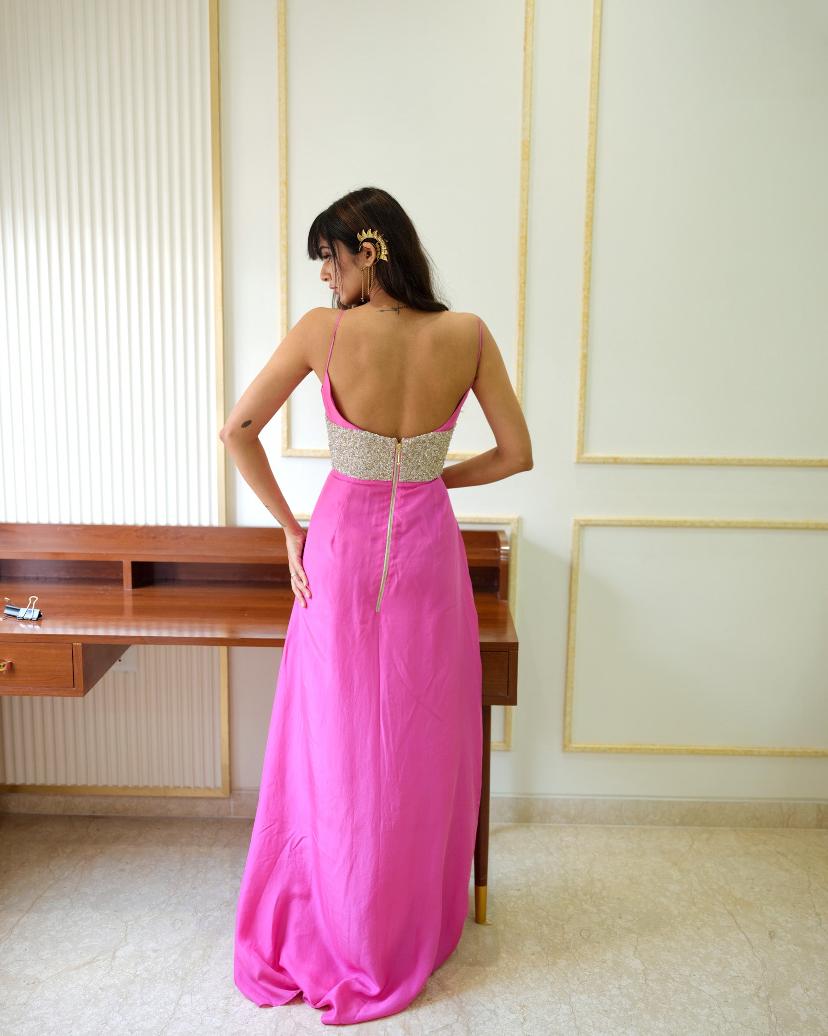 Woman in a pink evening gown with a high slit standing in a room.