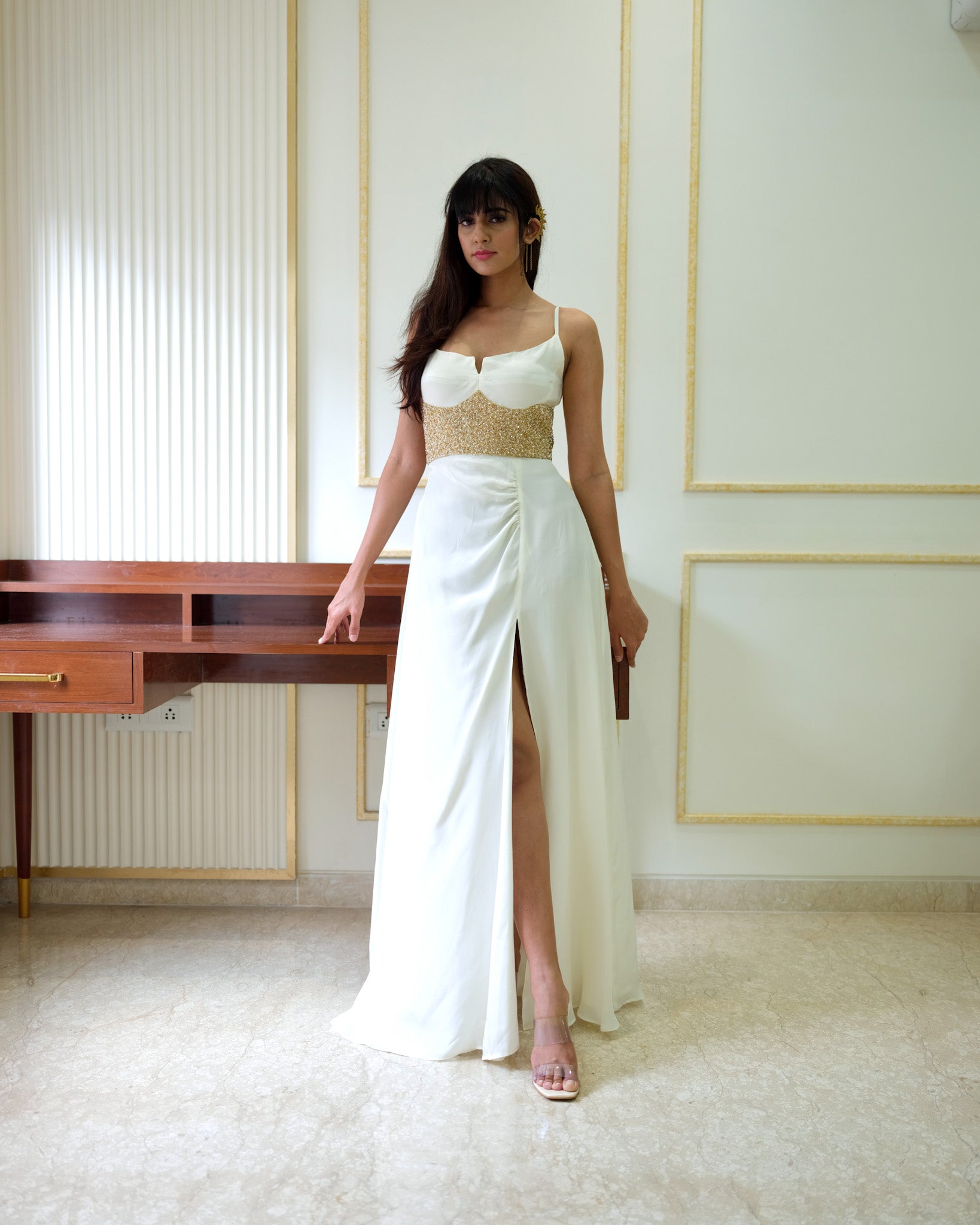 Woman wearing a white dress with a gold belt in an elegant room.