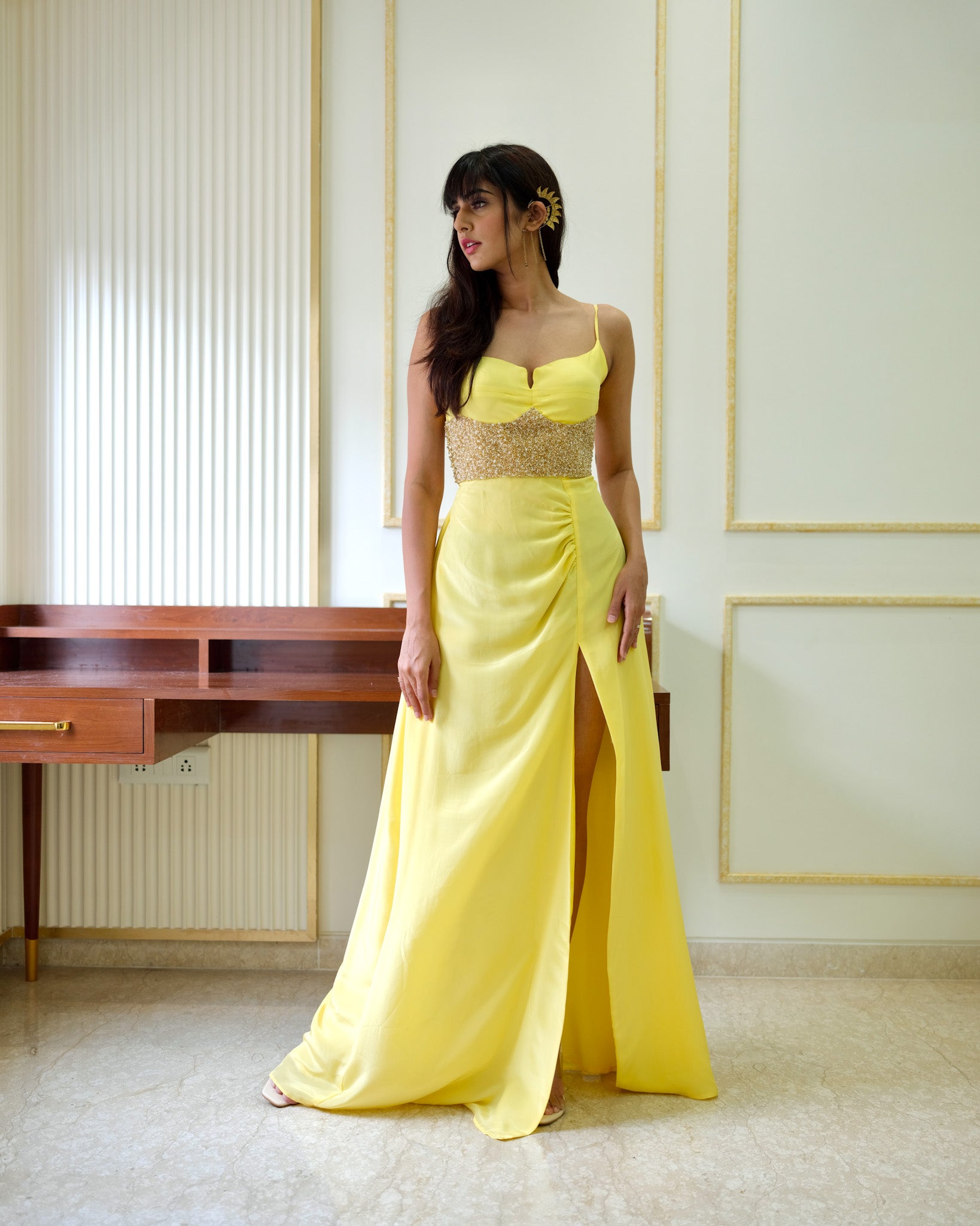 Woman in a yellow evening gown with a slit standing in an elegant room.