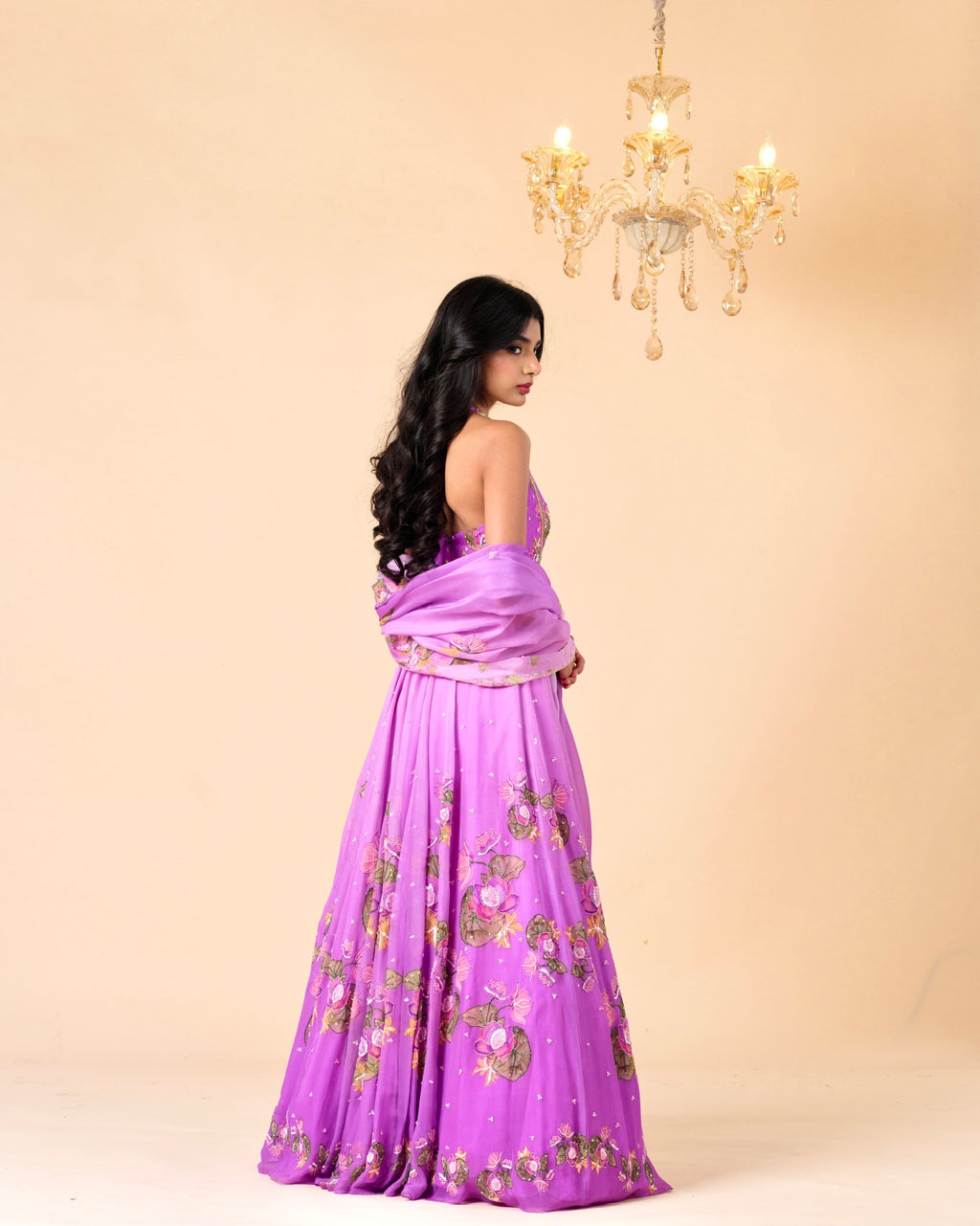 Woman in a purple saree with gold patterns against a beige background