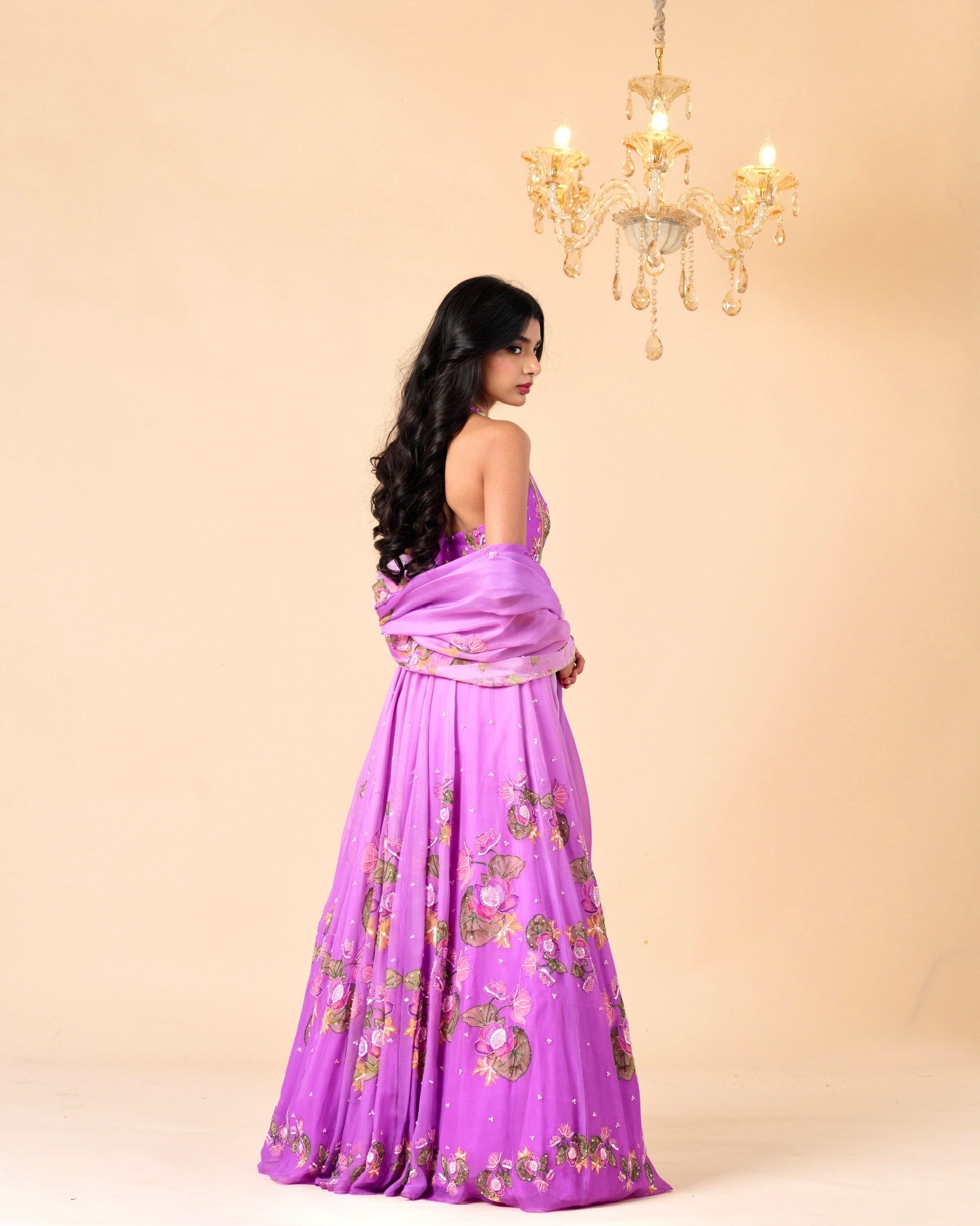 Woman in a purple saree with gold patterns against a beige background