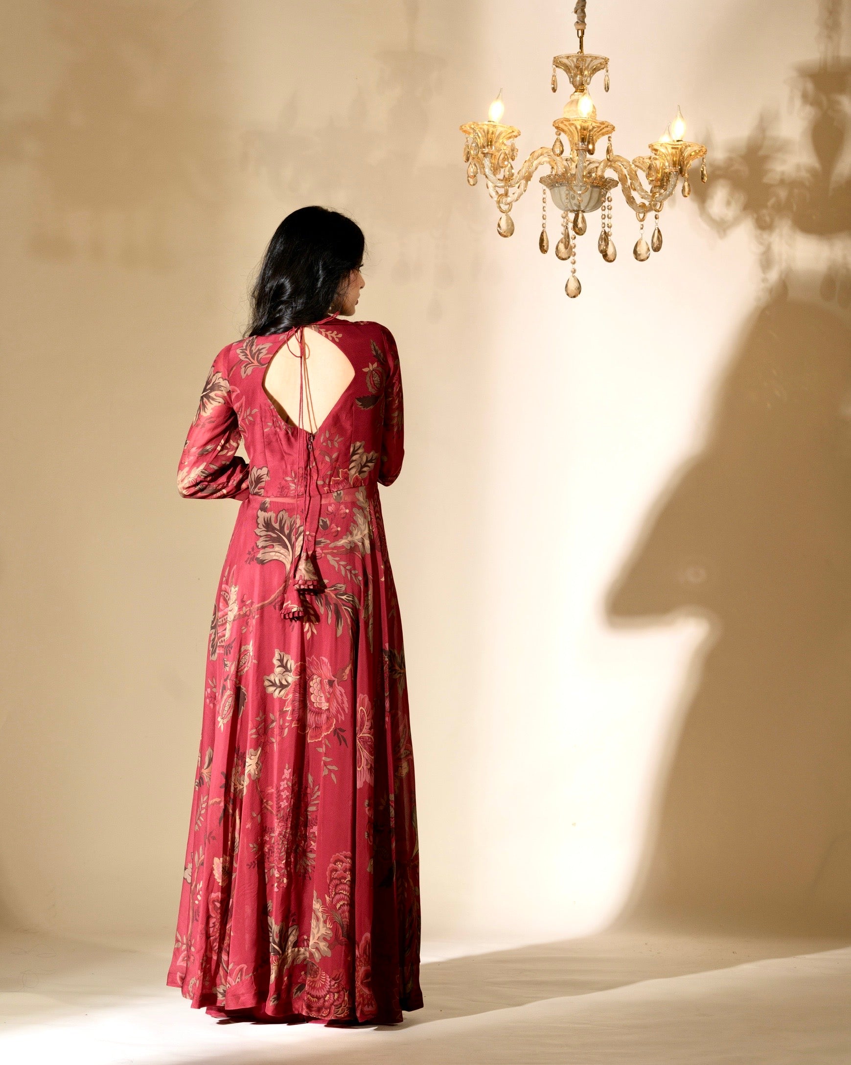 Woman in a red floral dress standing in front of a chandelier with a warm glow.