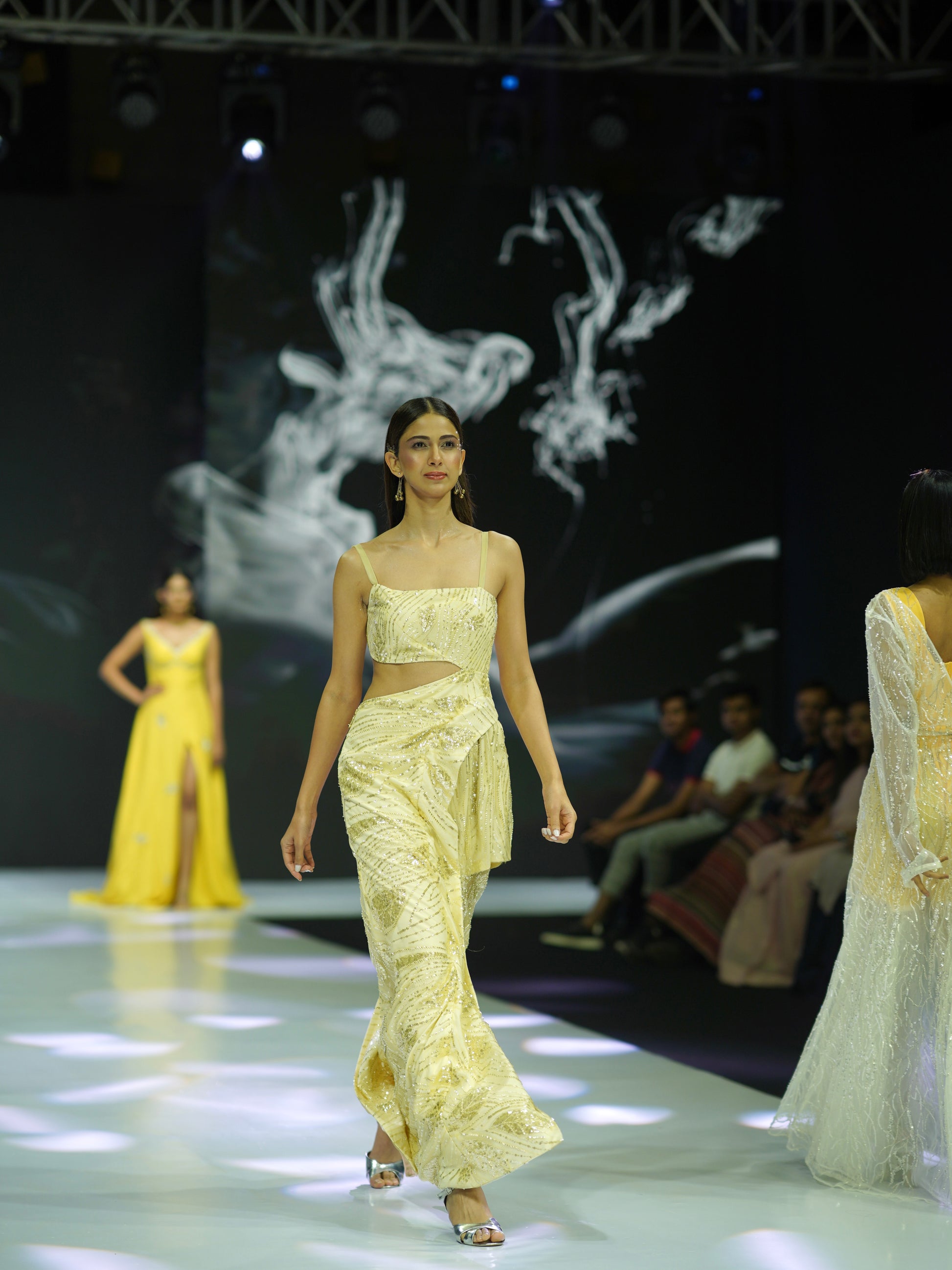 Model walking on a fashion show runway wearing a yellow outfit.