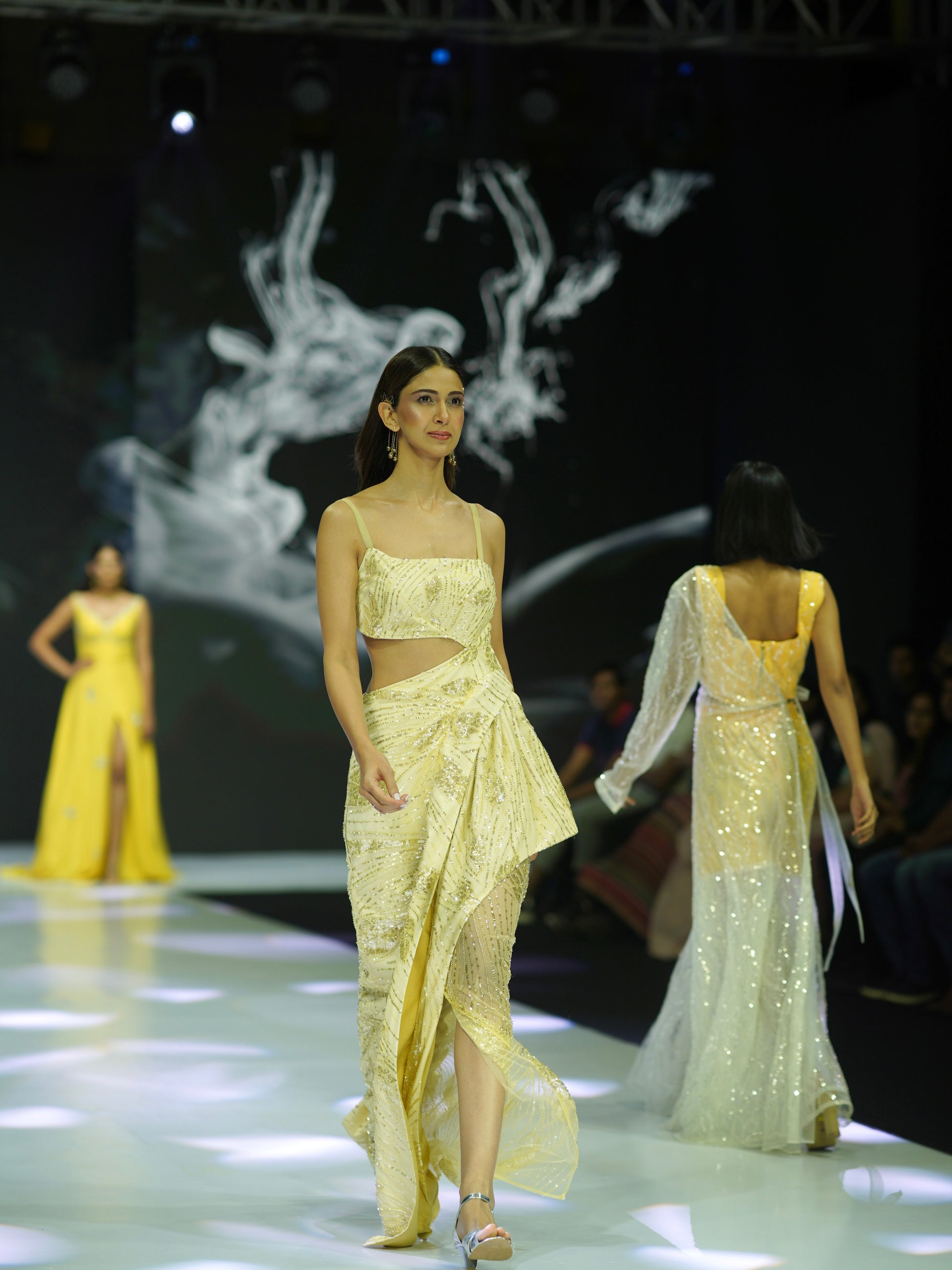 Model walking on a fashion show runway wearing a yellow outfit.