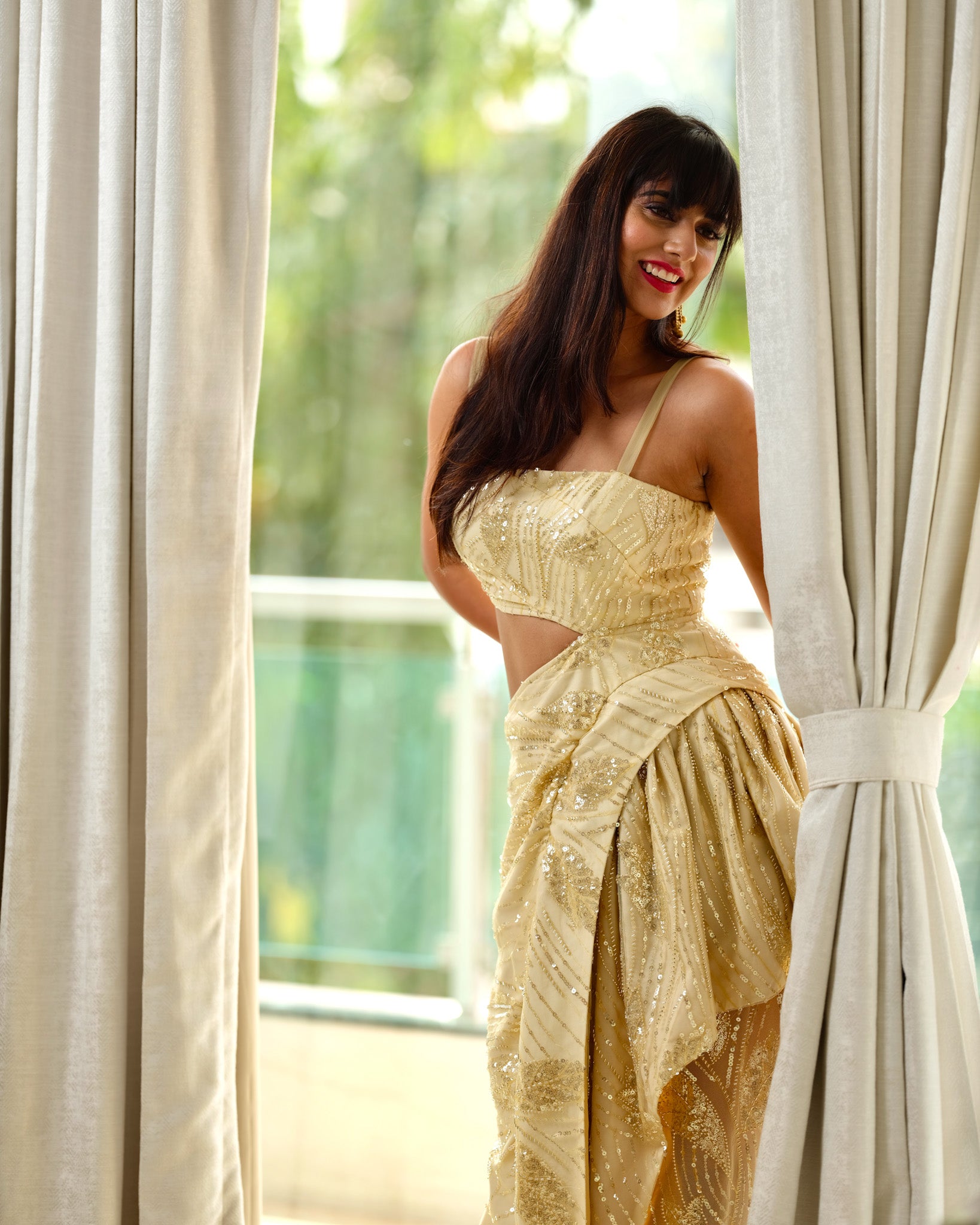 Woman in a yellow dress standing in front of a window with white curtains.
