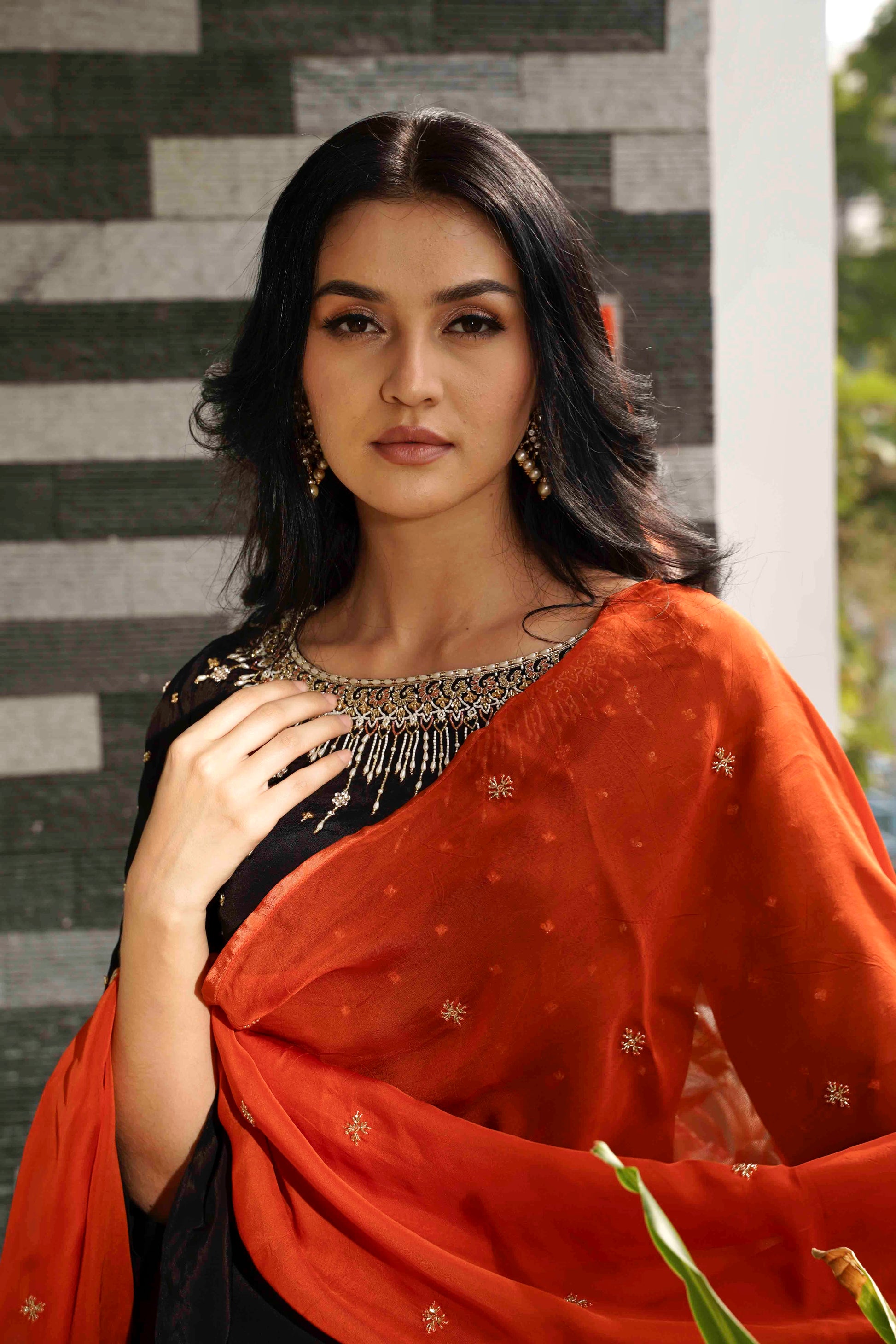 Woman wearing a traditional saree with a black and orange pattern against a stone wall.