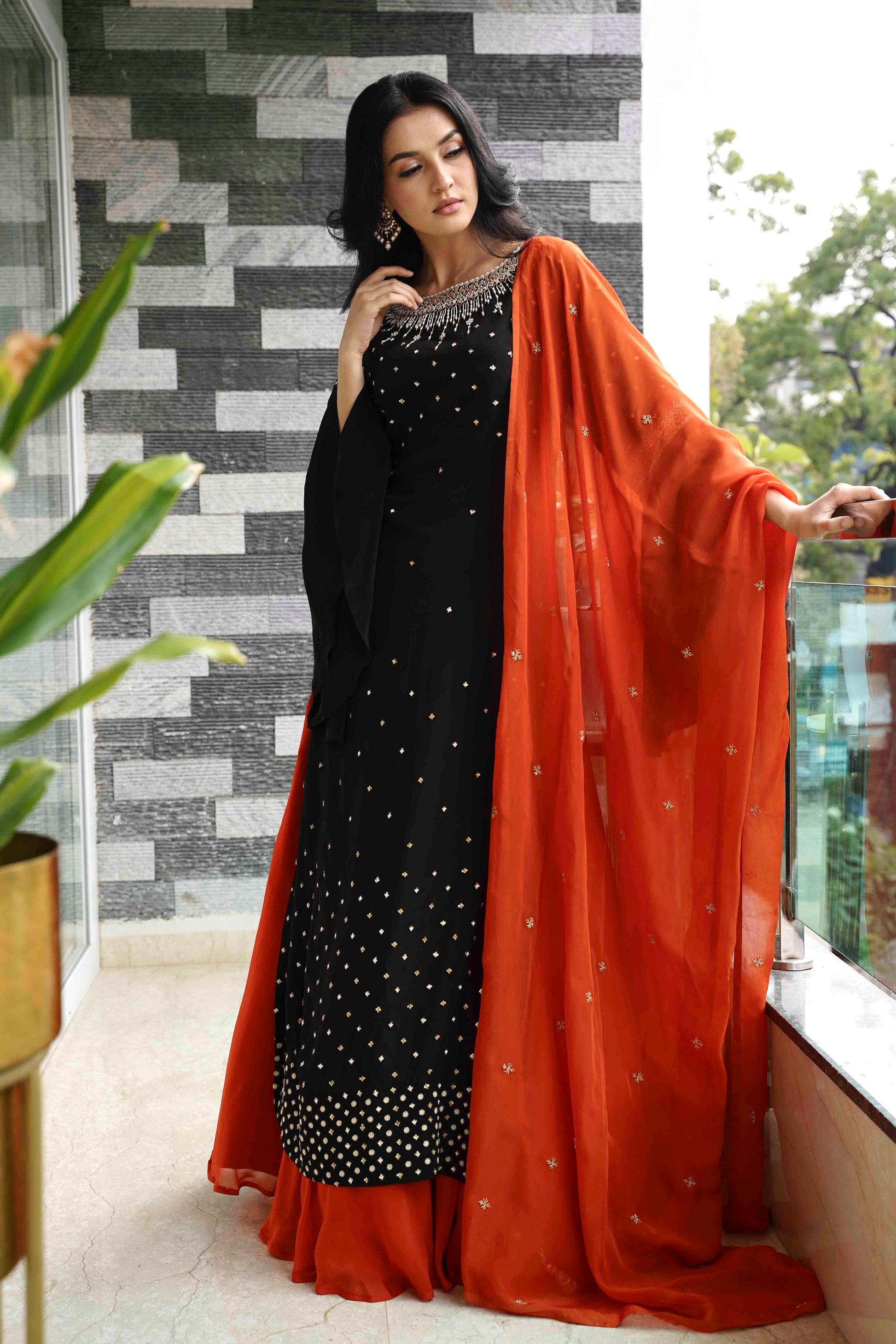 Woman in a black and white dress with an orange dupatta standing indoors.