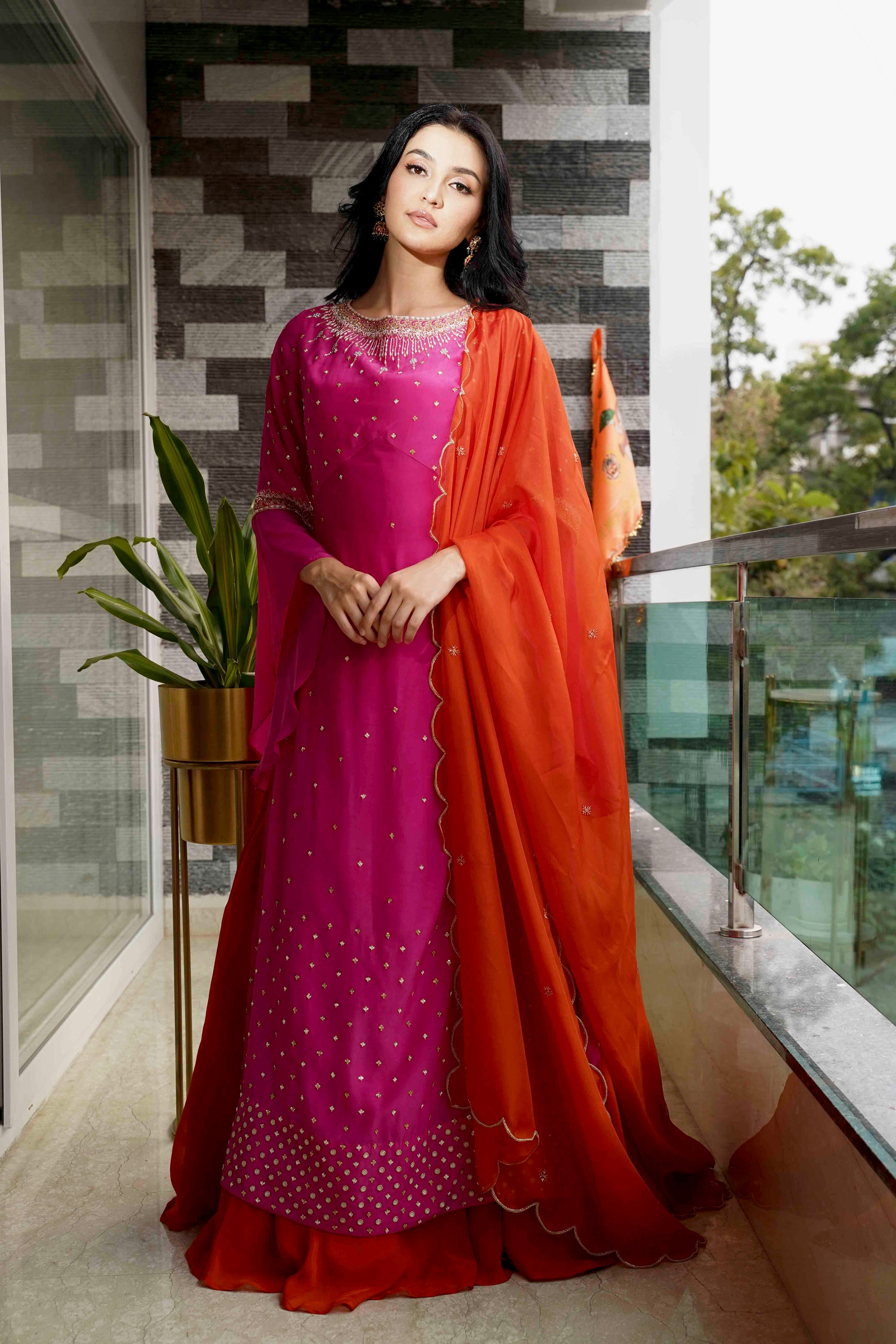 Woman in a pink and orange traditional outfit standing on a balcony.