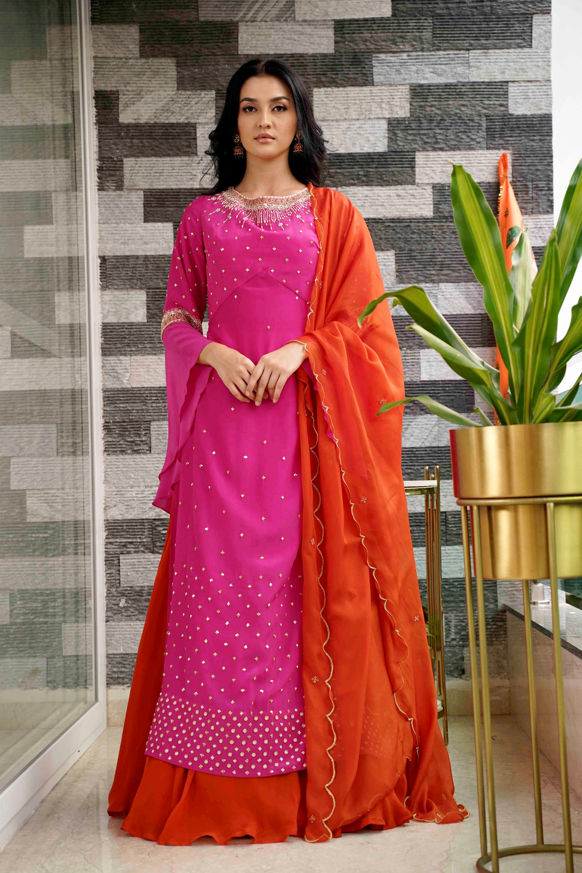 Woman wearing a pink and orange traditional outfit with a plant in the background