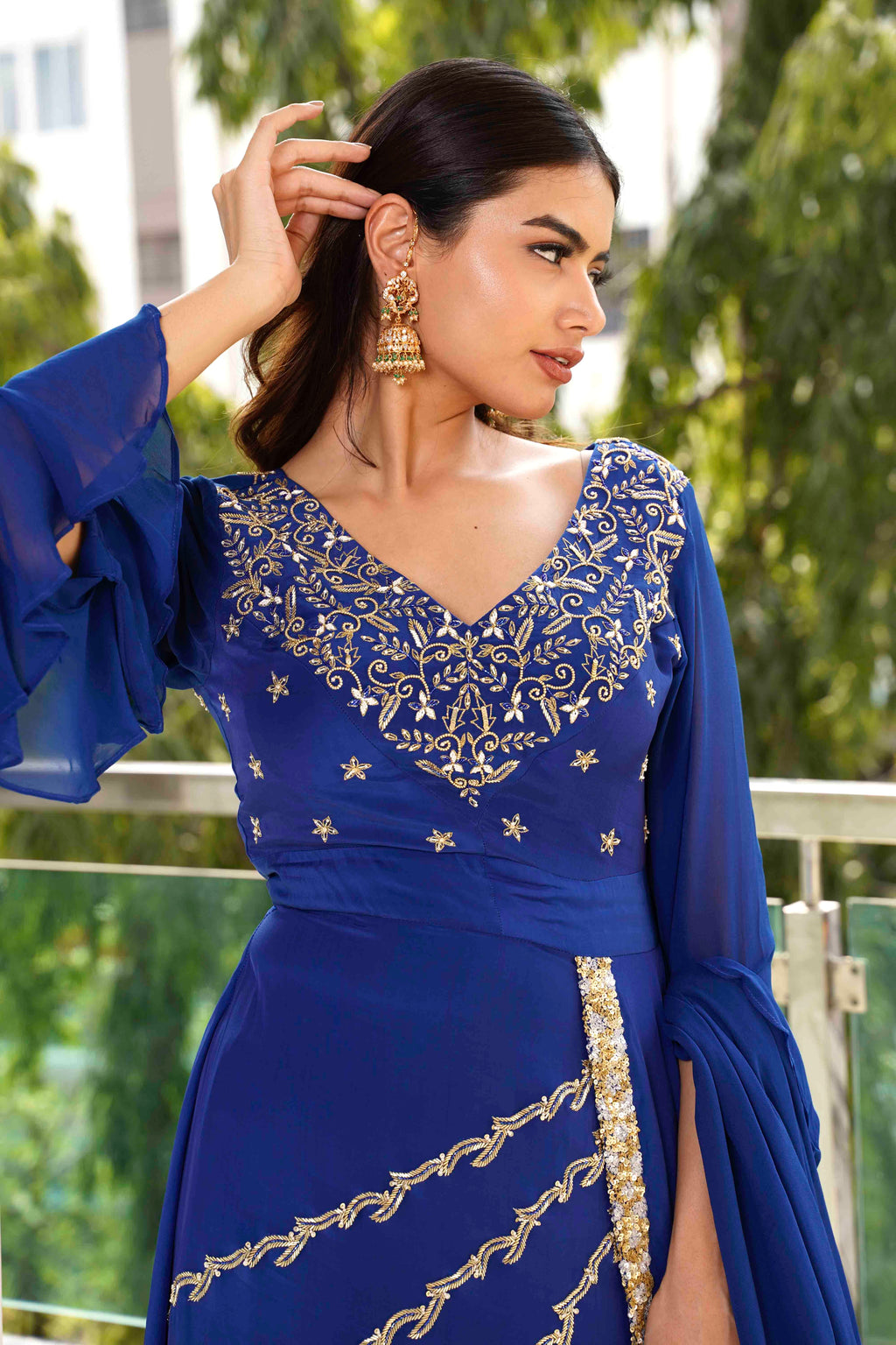Woman wearing a blue embroidered dress with gold details outdoors.