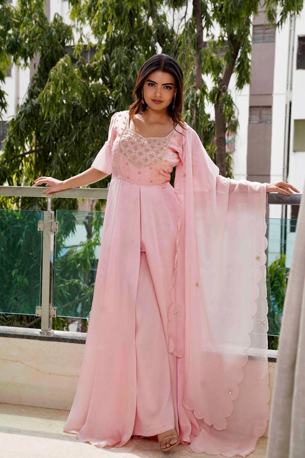 Woman in a pink traditional outfit standing on a balcony with greenery in the background
