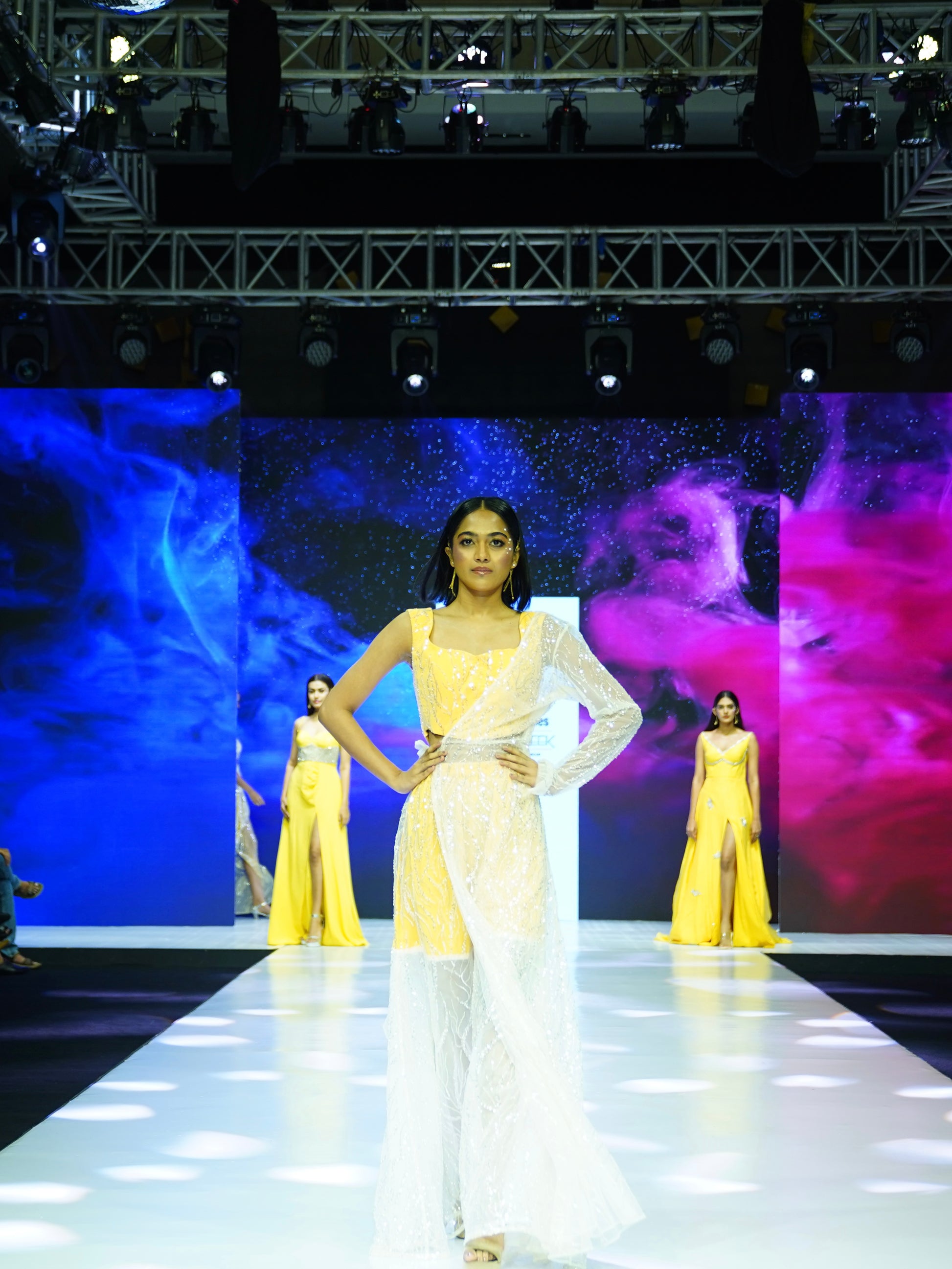 Model in a yellow dress walking on a runway with colorful background