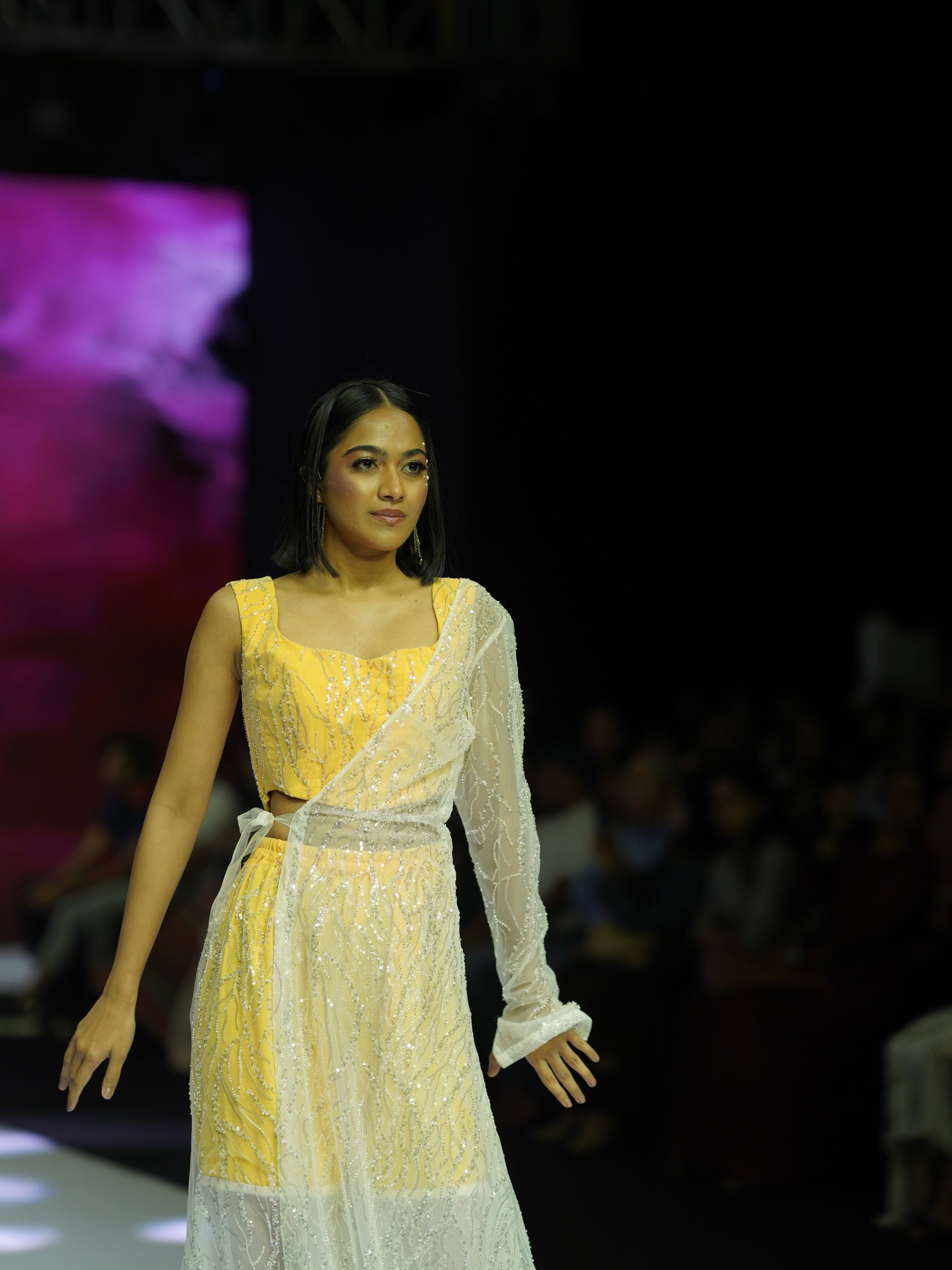Model wearing a yellow and white outfit on a fashion show runway.