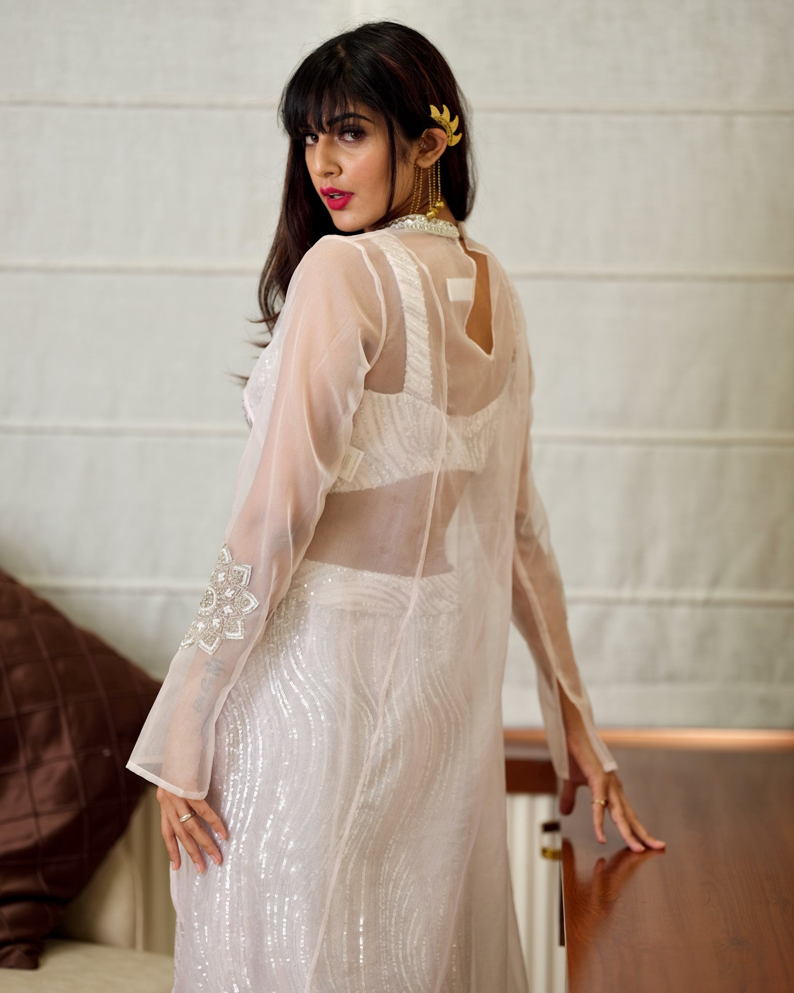 Woman wearing a white saree with a sheer blouse against a neutral background
