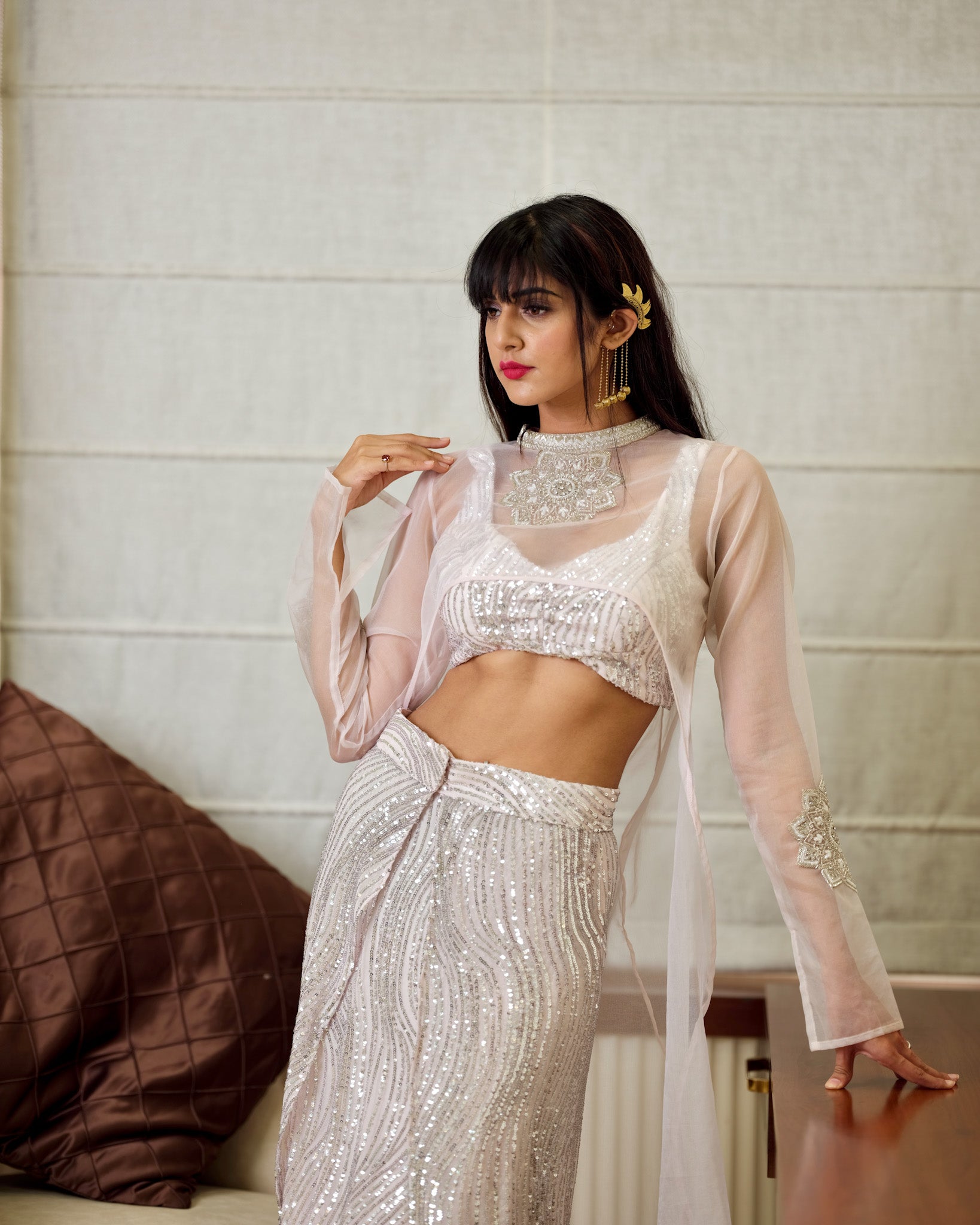 Woman in a white and silver traditional outfit with sheer sleeves indoors.