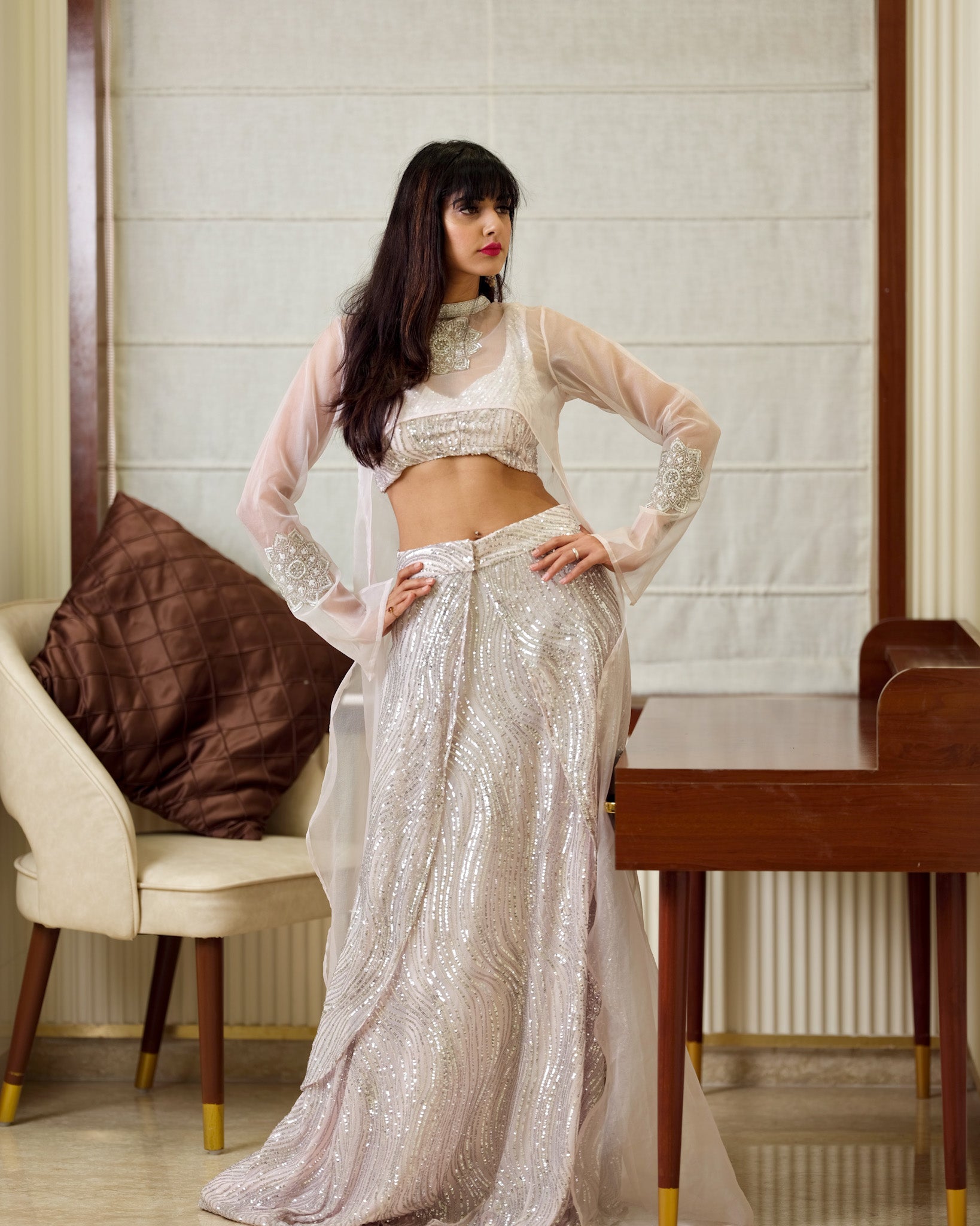 Woman in a sparkling silver outfit posing in an elegant room.
