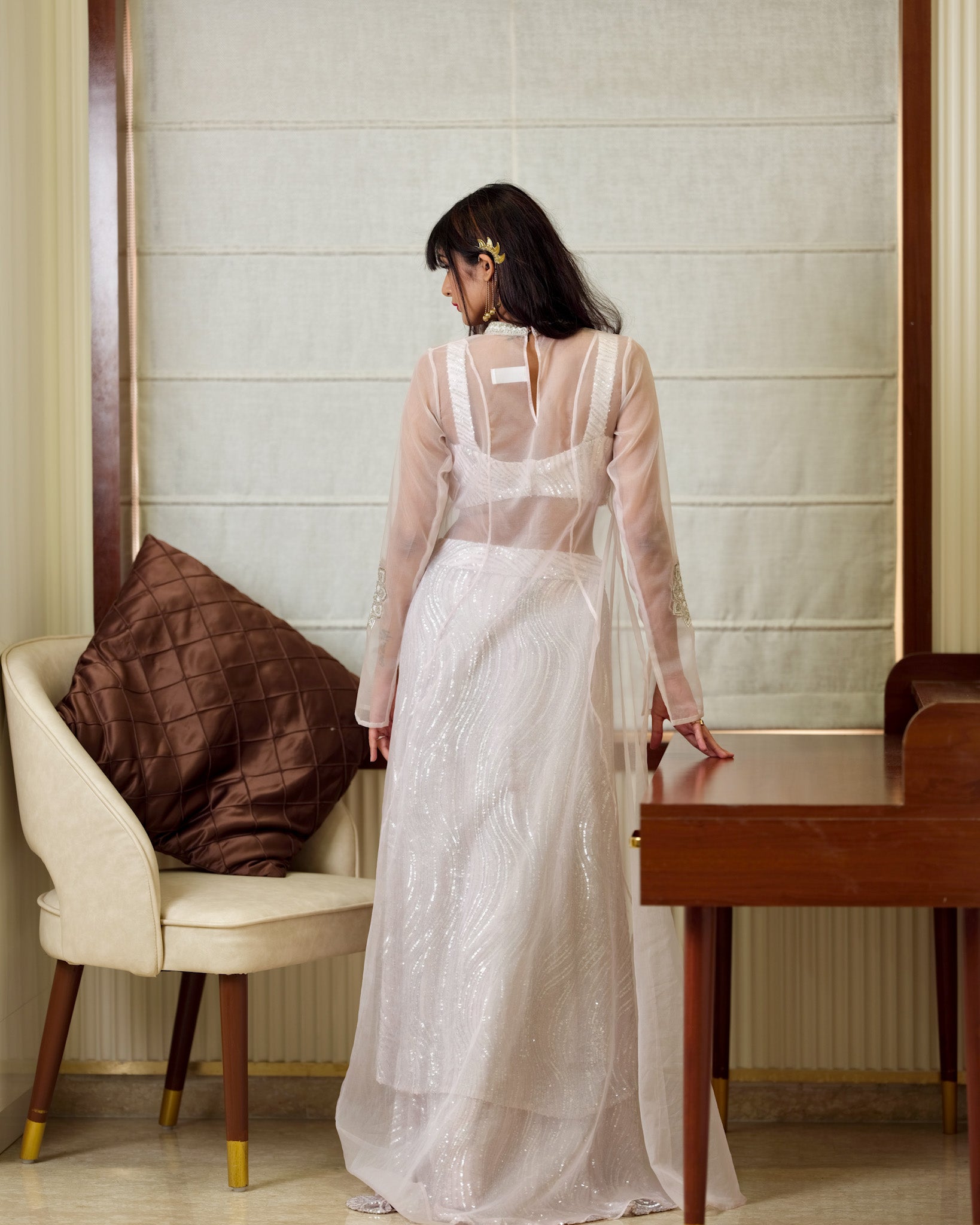 Woman in a white dress standing in a room with a chair and table.