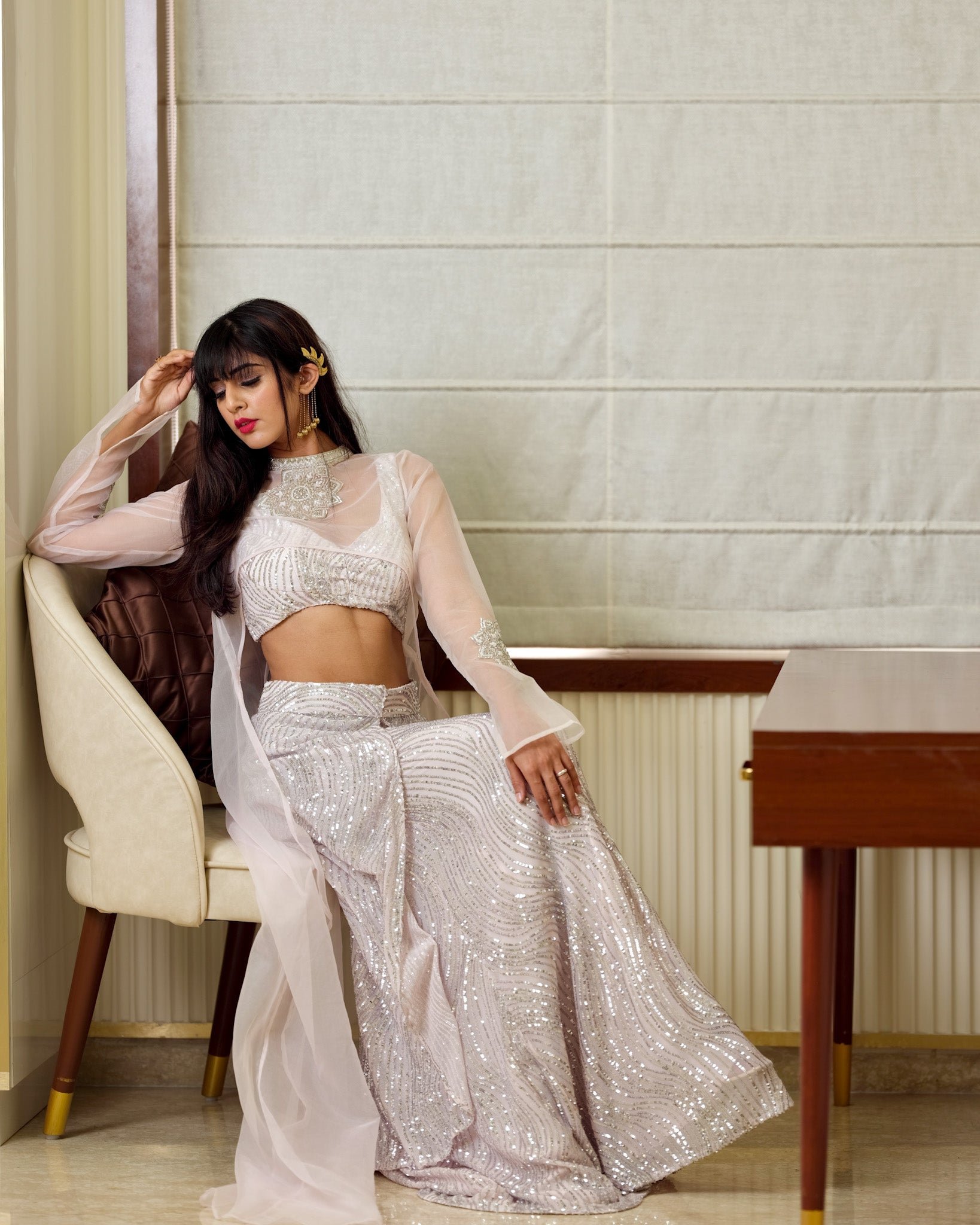 Woman in a silver traditional outfit sitting on a chair indoors.
