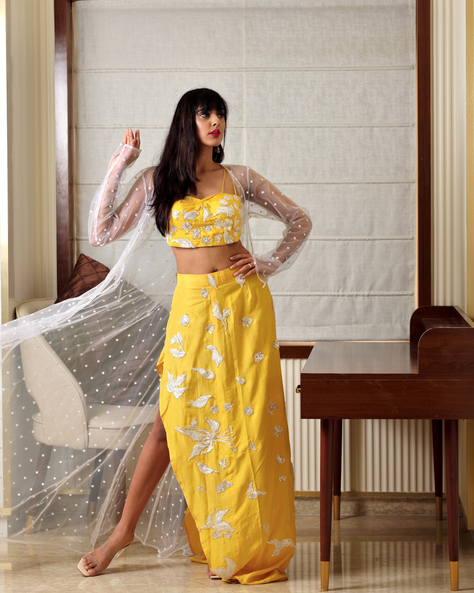 Woman in a yellow floral outfit standing indoors with a neutral background