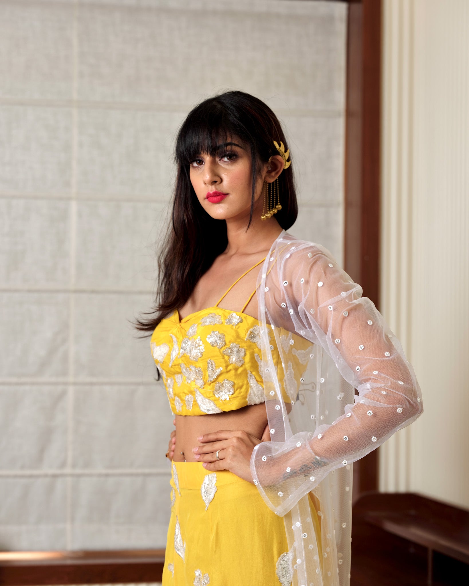 Woman wearing a yellow floral outfit with a sheer white overlay against a neutral background
