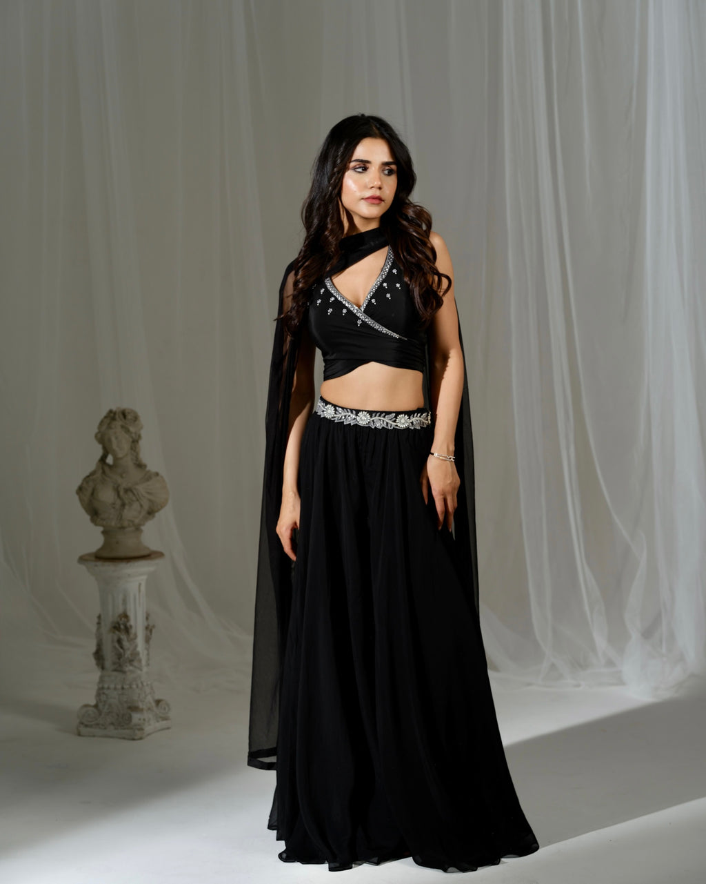 Woman wearing a black outfit with a sheer overlay against a white curtain background