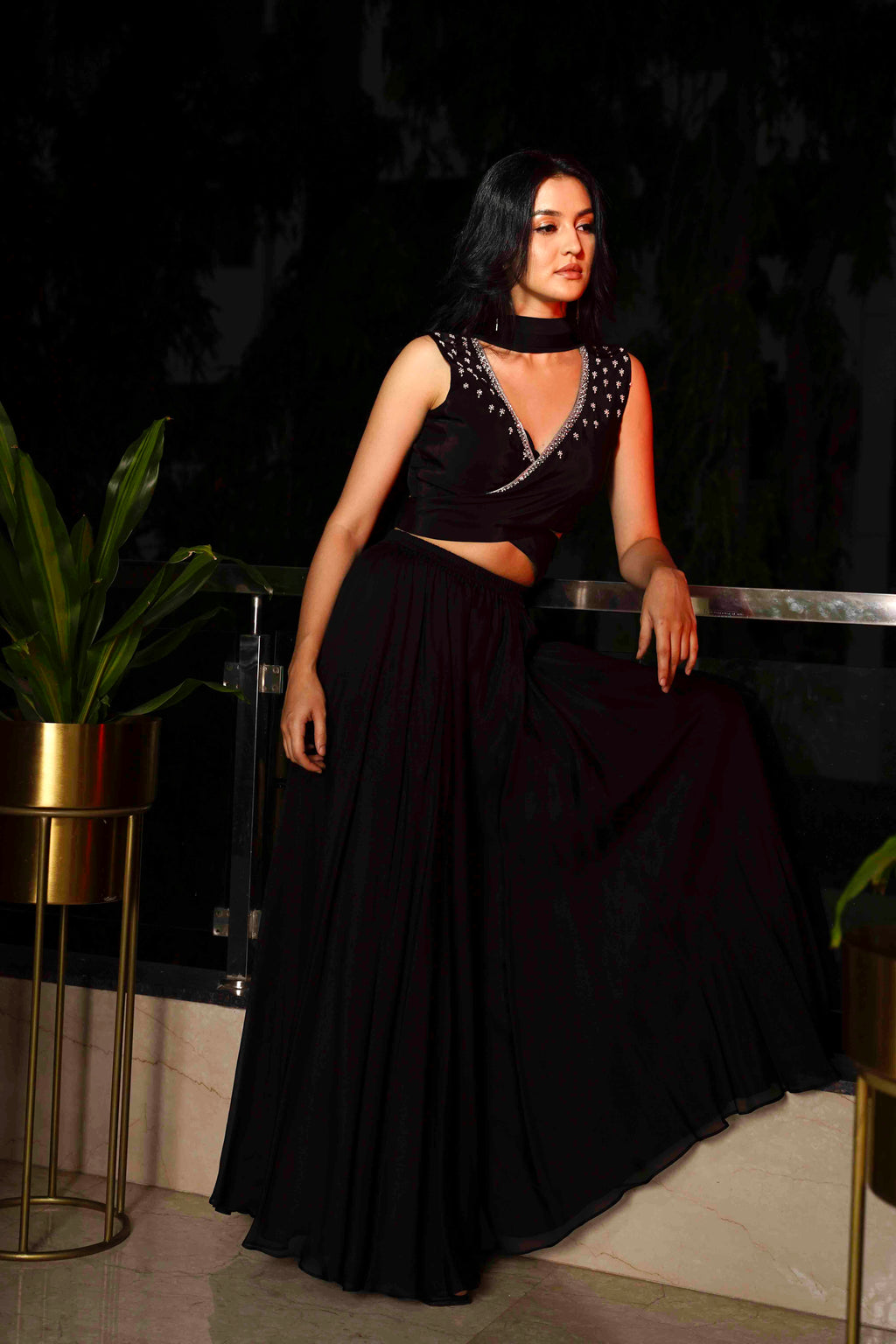 A woman modeling a black outfit with a structured cross-belt wrap blouse and voluminous pants, accessorized with a soft tulle dupatta.