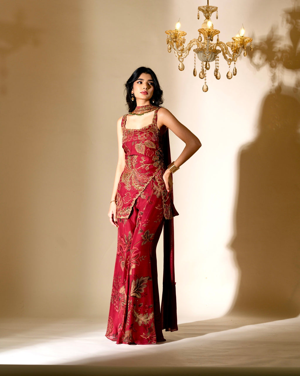 Woman in a red patterned dress standing in a softly lit room with a chandelier.