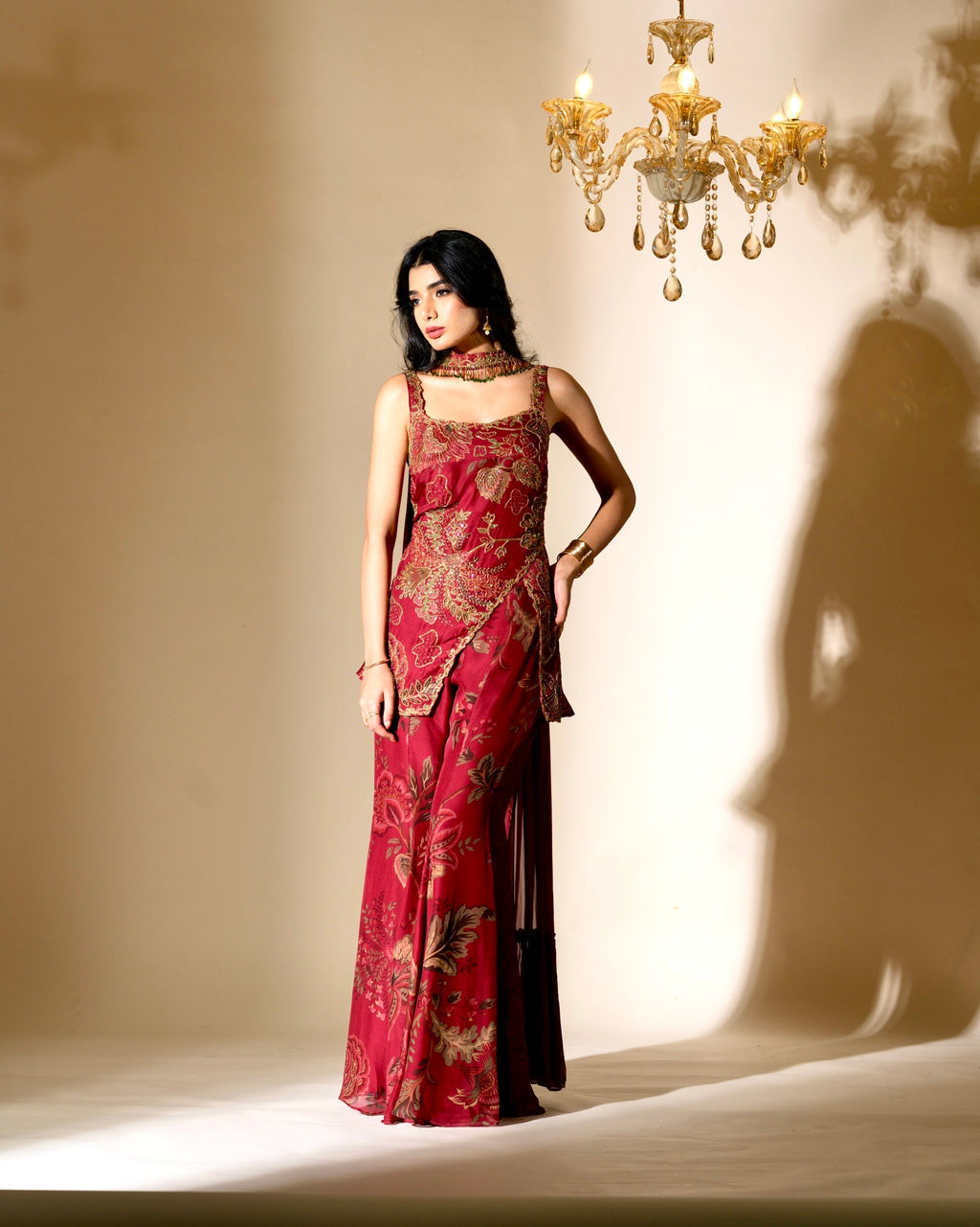 Woman in a red and gold dress standing in front of a chandelier