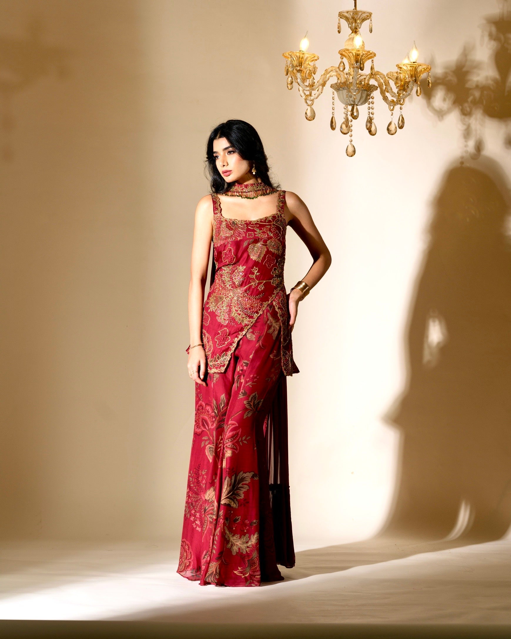 Woman in a red and gold dress standing in front of a chandelier