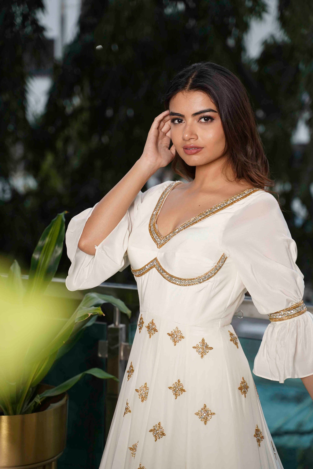 Woman wearing a white dress with gold embroidery against a blurred natural background