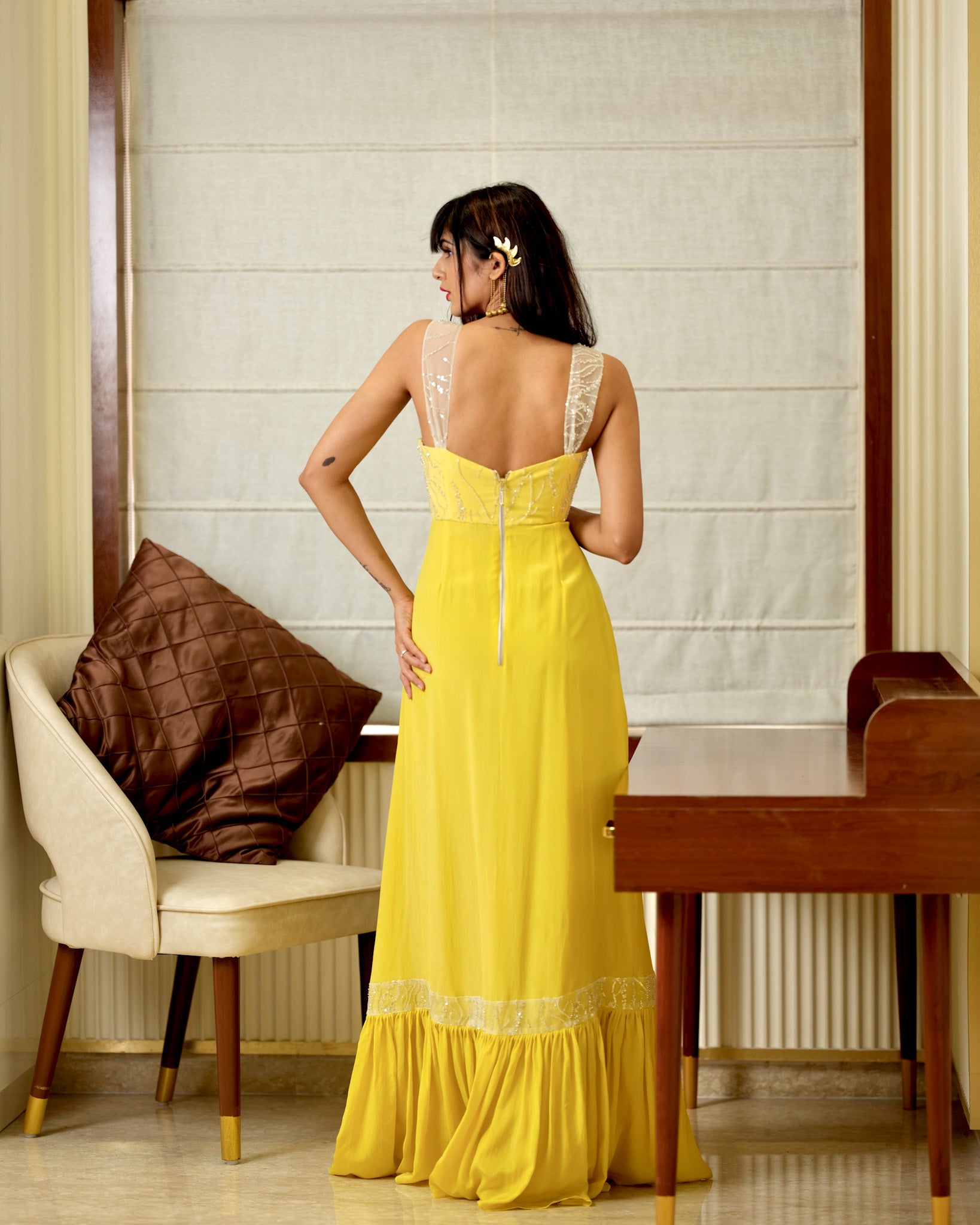Woman in a yellow dress standing in a room with a chair and table.