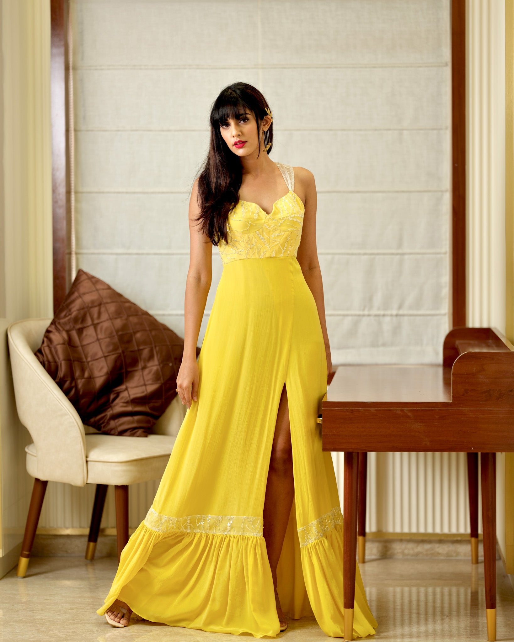Woman in a yellow dress standing in a room with a chair and table.