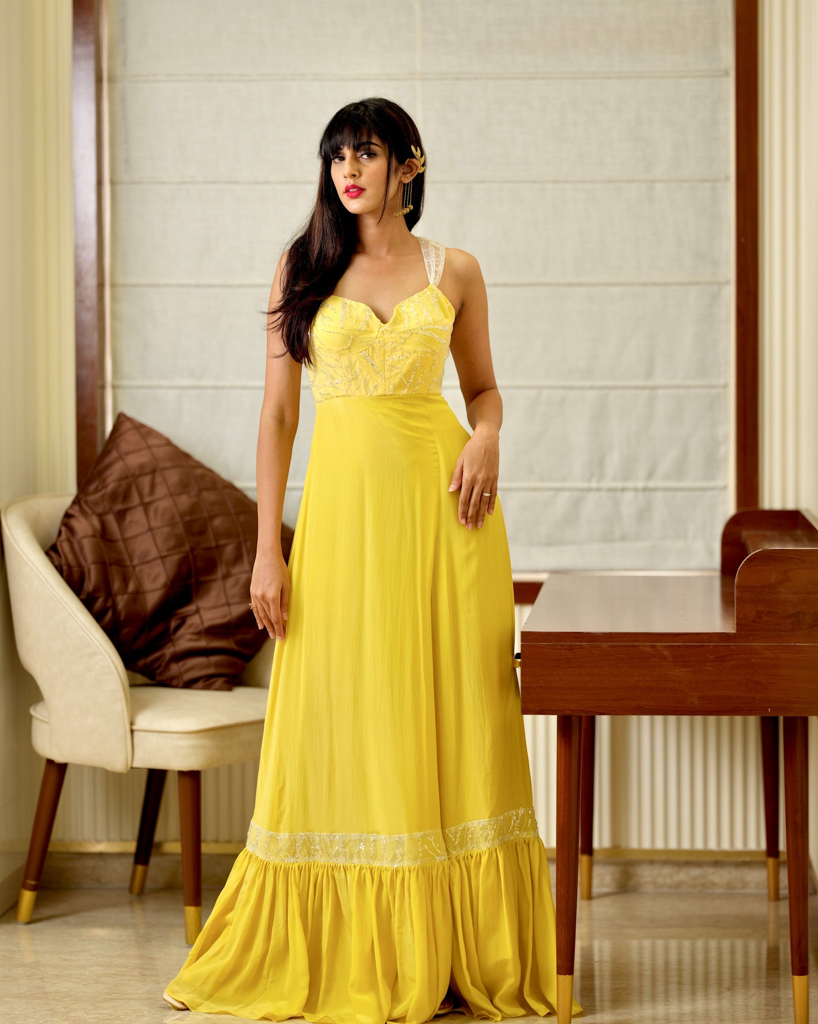 Woman in a yellow dress standing in a room with a chair and table.