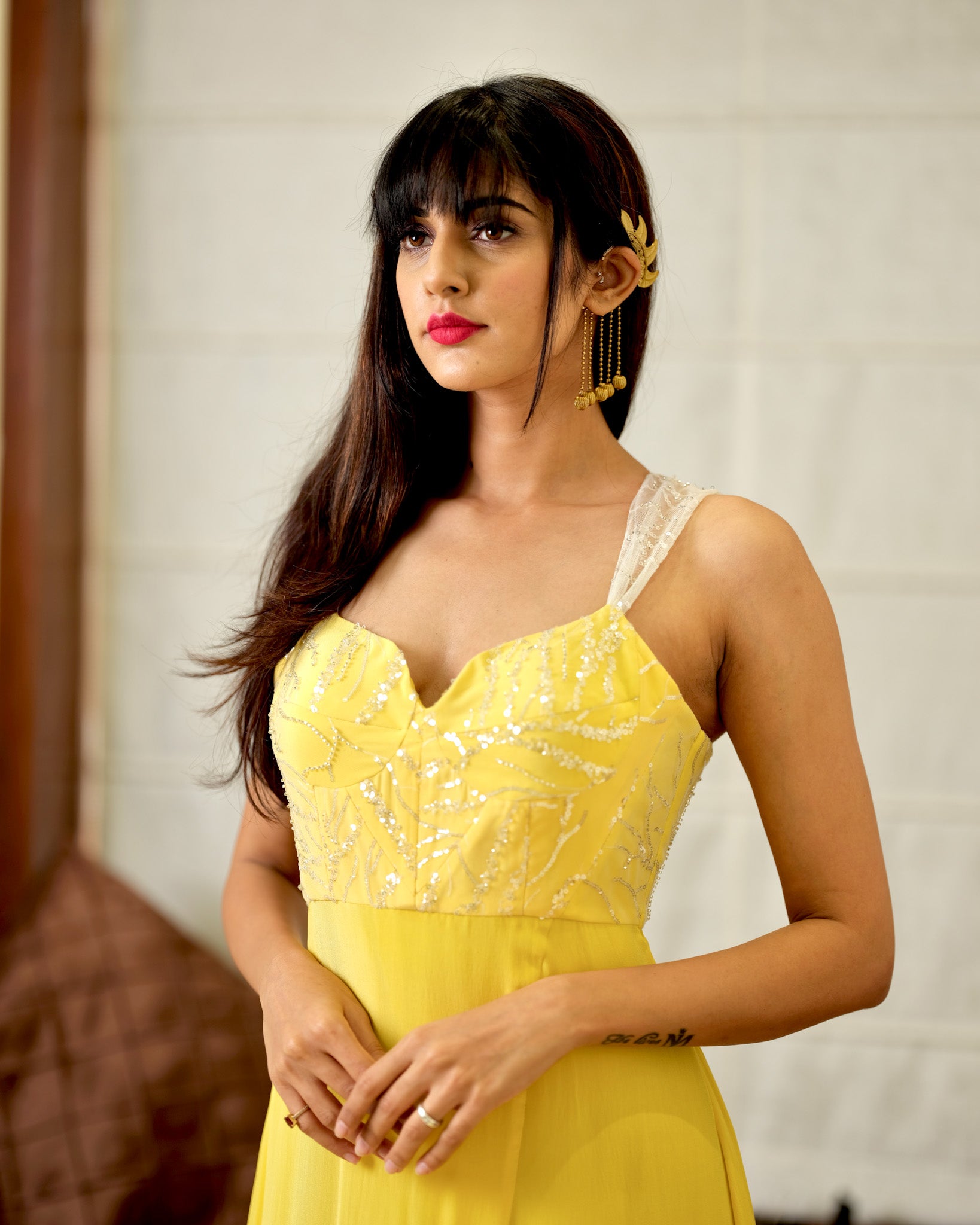 Woman wearing a yellow dress with intricate detailing against a neutral background