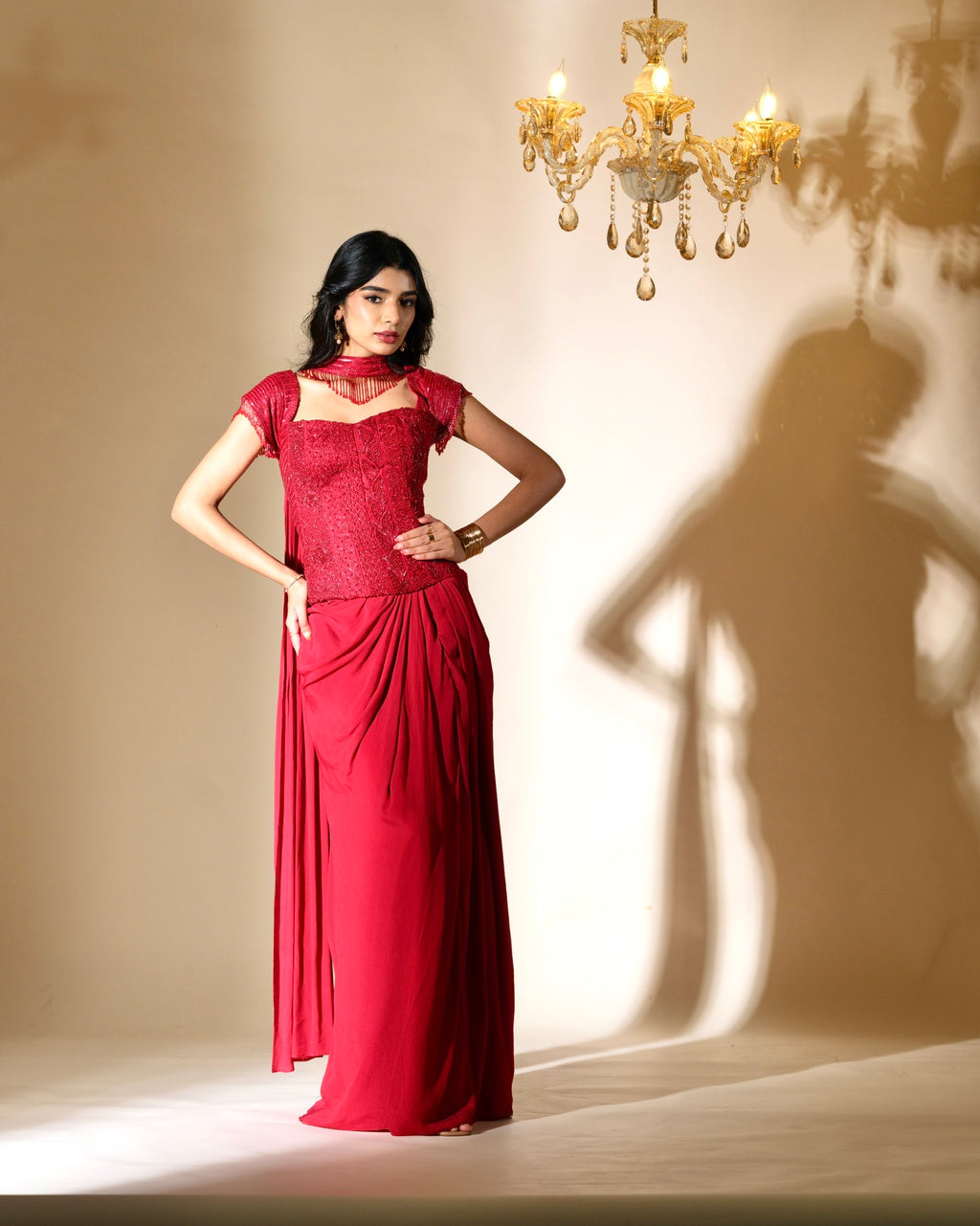 Woman in a red dress standing in front of a chandelier casting a shadow on the wall.