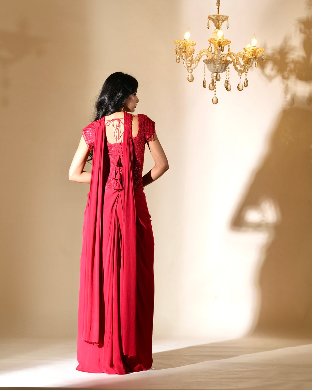 Woman in a red dress standing in front of a chandelier with a beige wall.