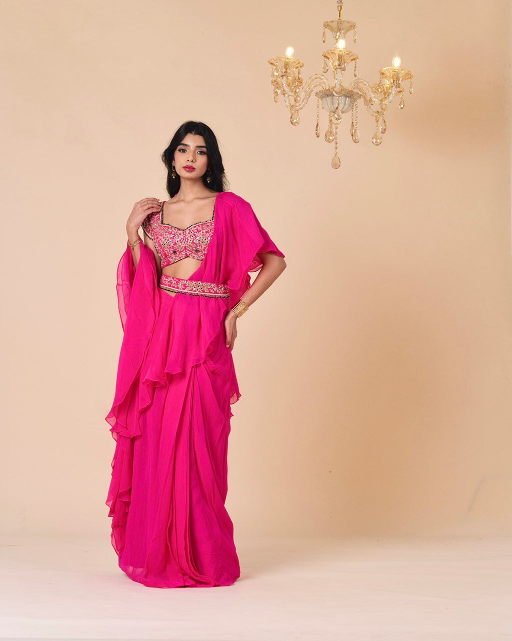 Woman wearing a bright pink saree with a matching blouse against a beige background