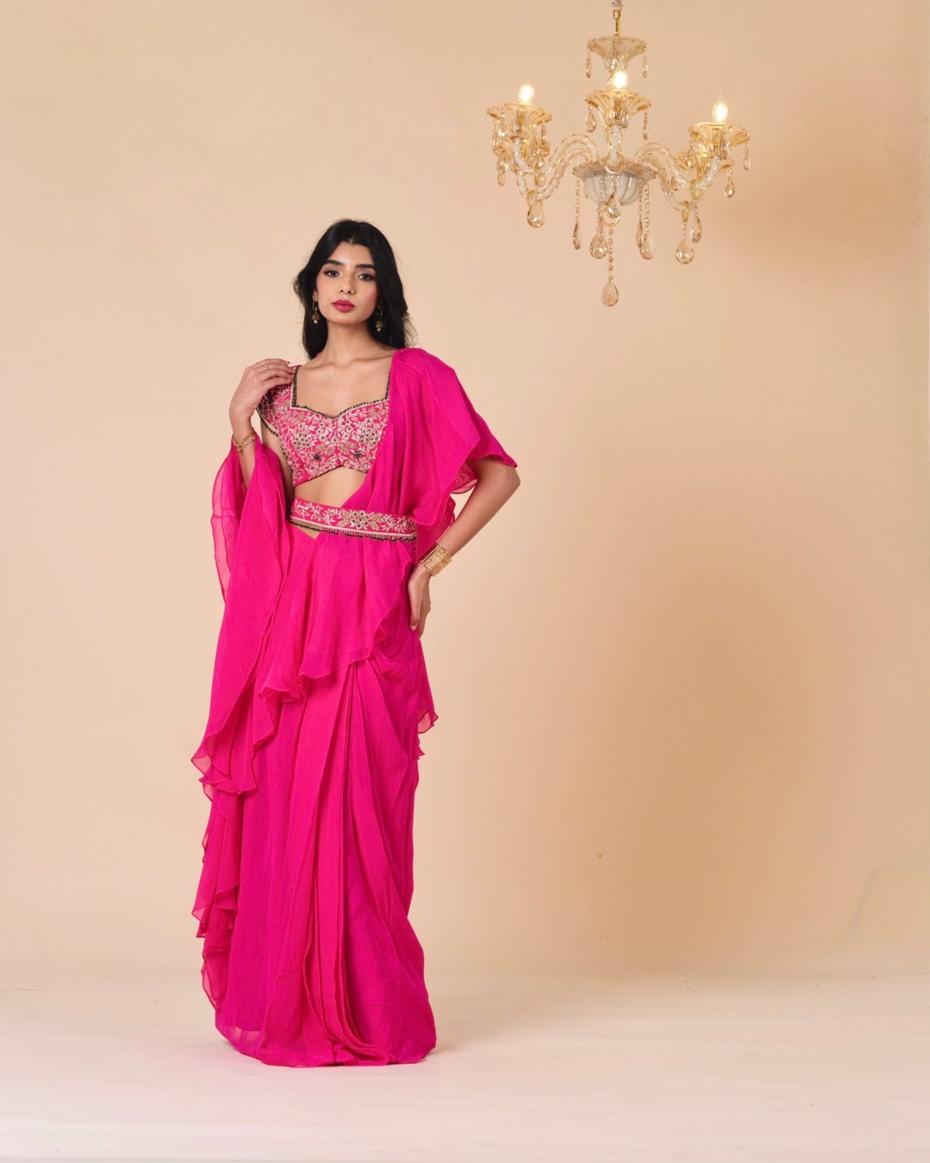 Woman wearing a bright pink saree with a matching blouse against a beige background