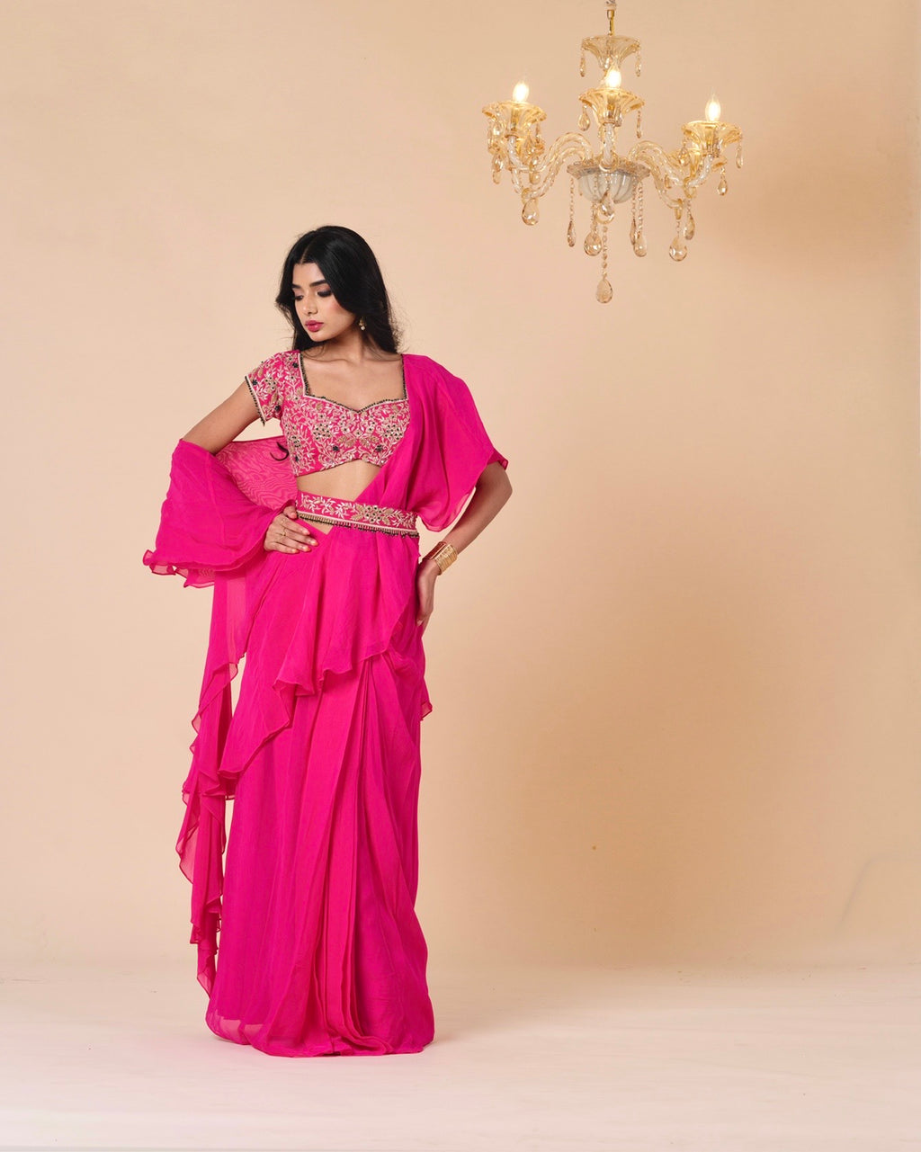 Woman wearing a bright pink saree with a matching blouse against a beige background