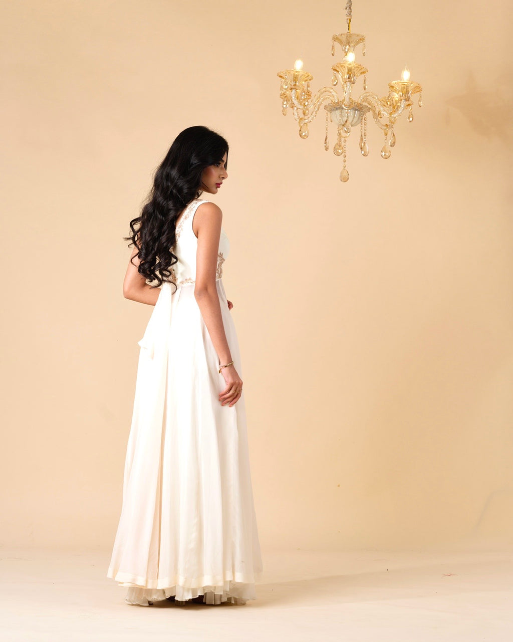 Woman in a white dress standing in a room with a chandelier.