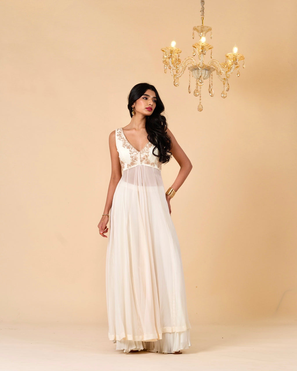 Woman wearing a white dress with gold detailing against a beige background