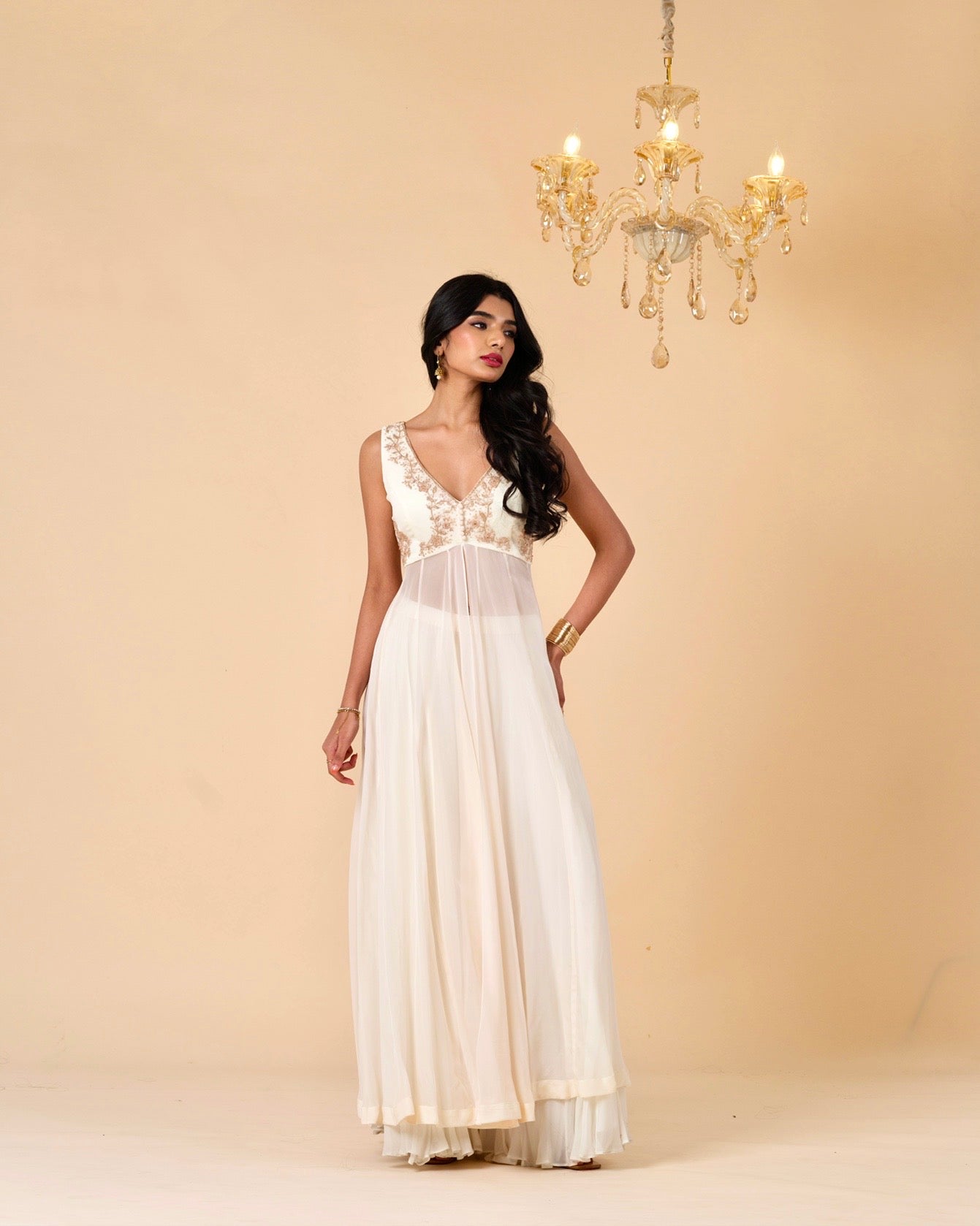 Woman wearing a white dress with gold detailing against a beige background