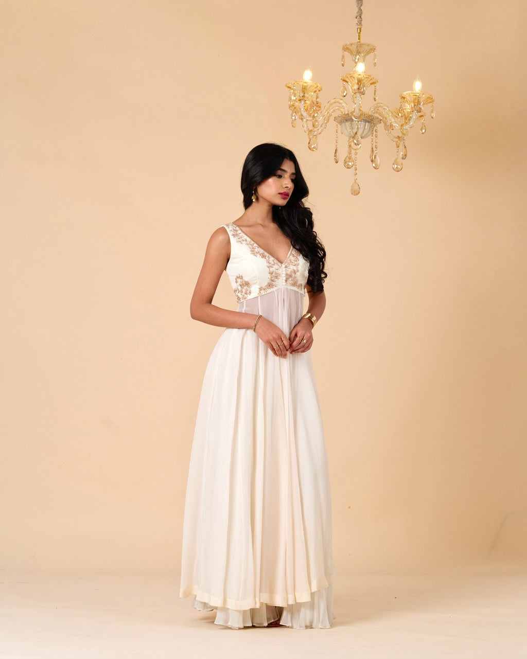 Woman wearing a white evening gown against a beige background with a chandelier.