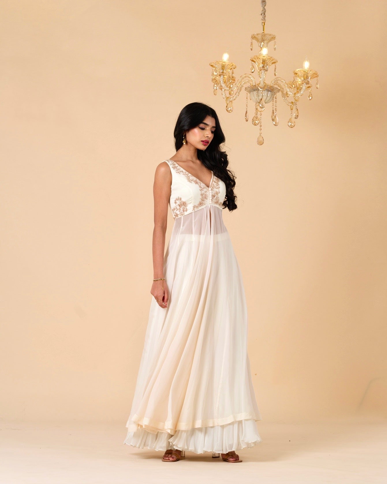 Woman in a white dress standing in front of a beige wall with a chandelier.